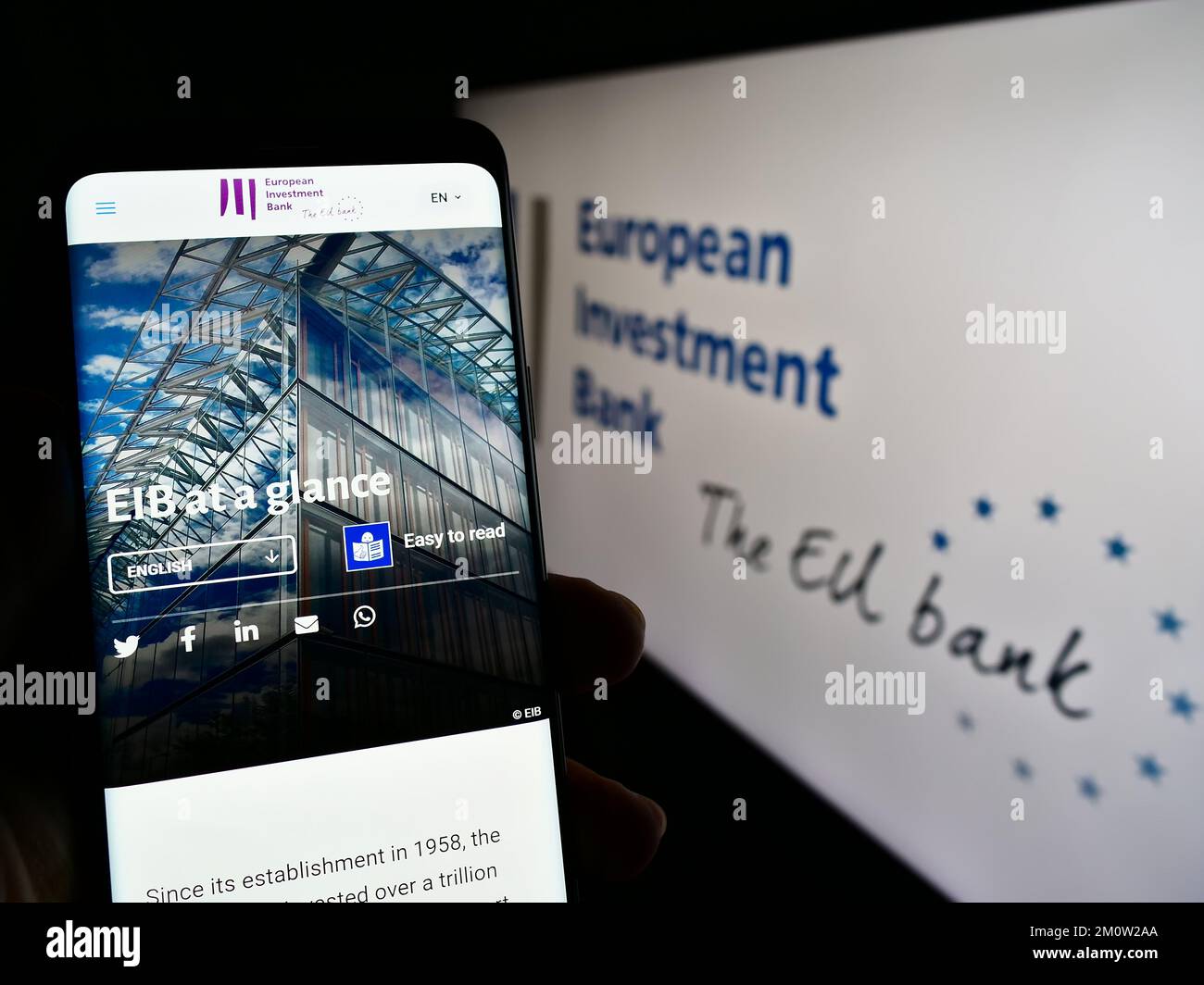 Personne tenant un téléphone portable avec page web de l'institution de l'UE Banque européenne d'investissement (BEI) à l'écran avec logo. Concentrez-vous sur le centre de l'écran du téléphone. Banque D'Images
