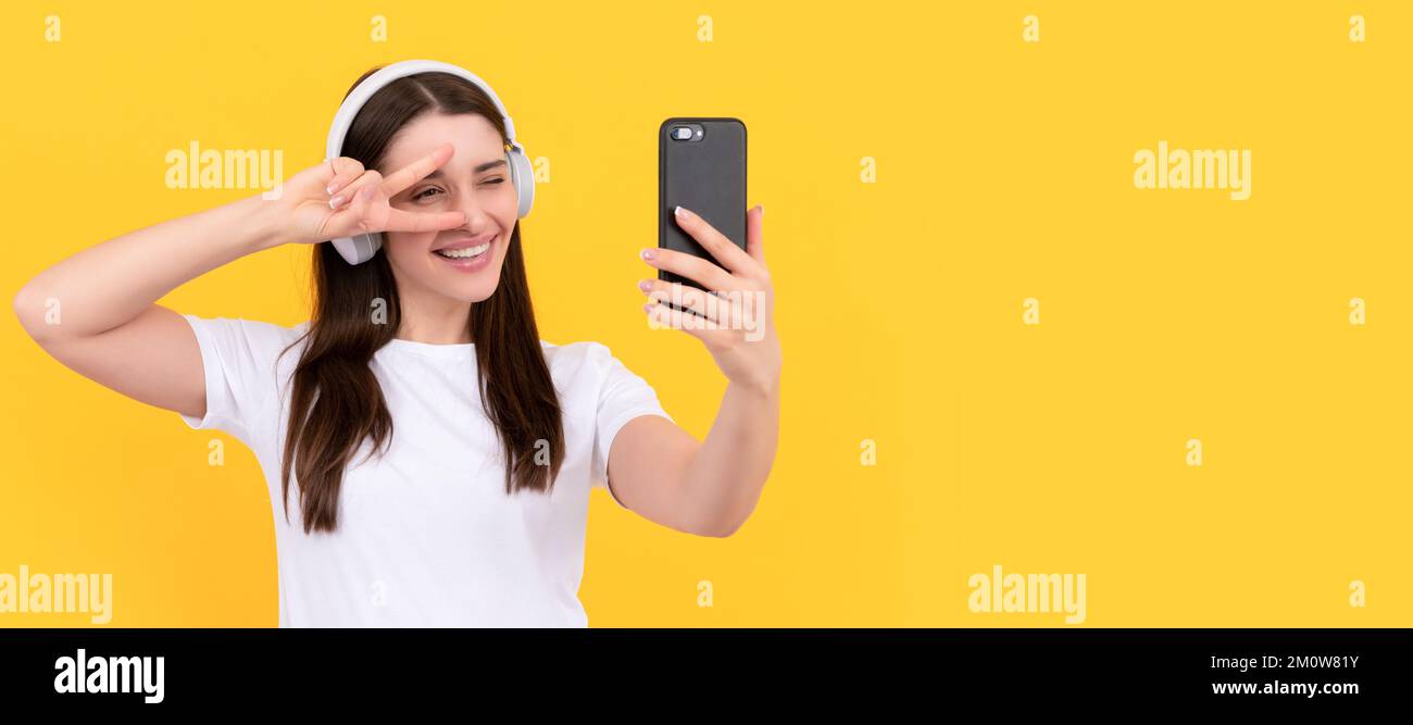 femme positive en chemise blanche dans le casque faisant selfie sur le téléphone avec le geste de paix, selfie. Femme isolée visage portrait, bannière avec espace de copie. Banque D'Images