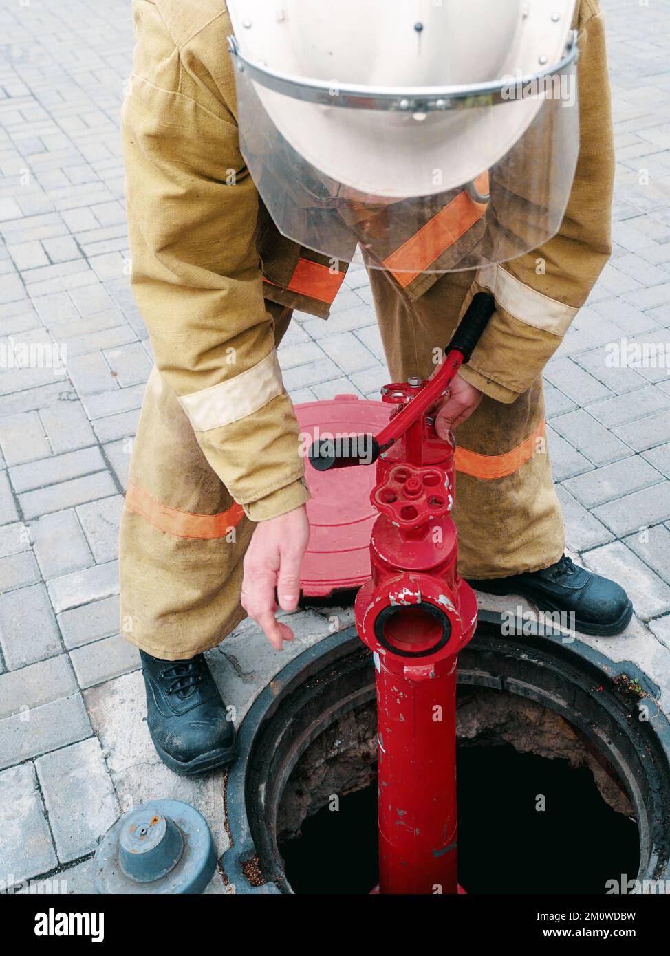 Un pompier ou un secouriste installe une borne incendie dans un puits ouvert. Travail de pompier en cas d'incendie. La formation et la pratique des actions en cas d'incendie. Arrière-plan... Banque D'Images
