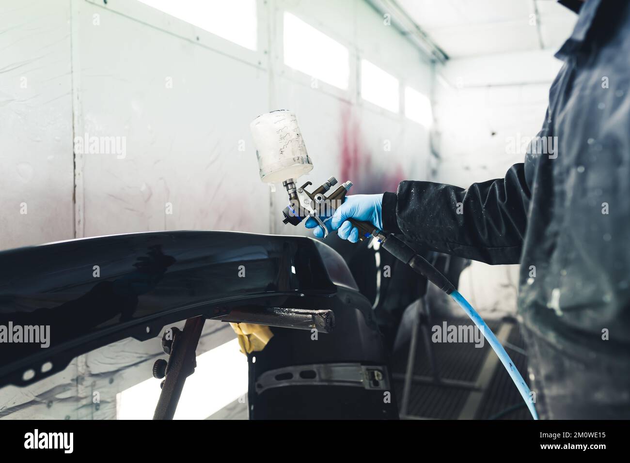 Intérieur de cabine de pulvérisation blanche. Procédé de peinture automobile. Vernissage des ailes de voiture. Personne non reconnaissable dans une combinaison de protection à l'aide d'un pistolet à peinture. Photo de haute qualité Banque D'Images