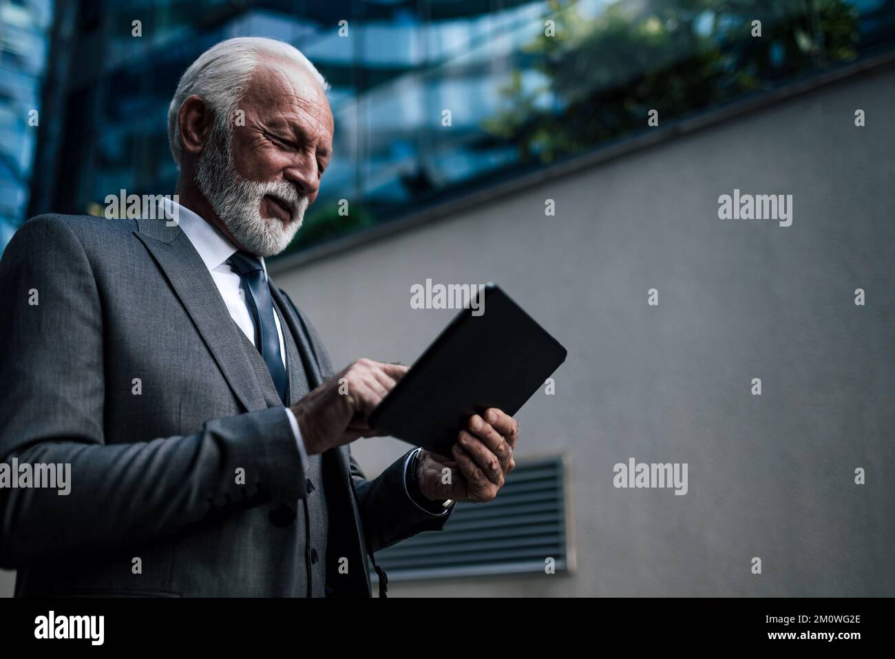 Homme d'affaires confiant analysant des idées sur une tablette numérique. Homme d'affaires souriant, vêtu d'un ordinateur sans fil. Il se tient contre les offi Banque D'Images