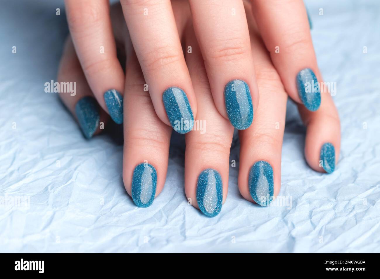 Mains de femmes avec une belle manucure - ongles bleus scintillants sur papier bleu froissé. Concept de soin des ongles Banque D'Images