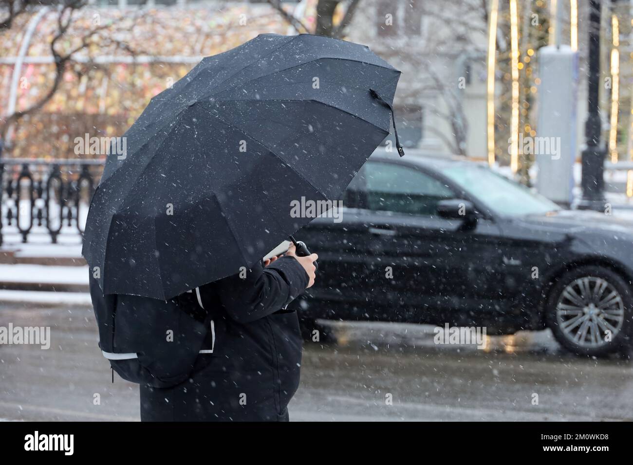 Neige avec pluie en ville d'hiver, femme avec parapluie debout sur une rue sur fond de voiture Banque D'Images