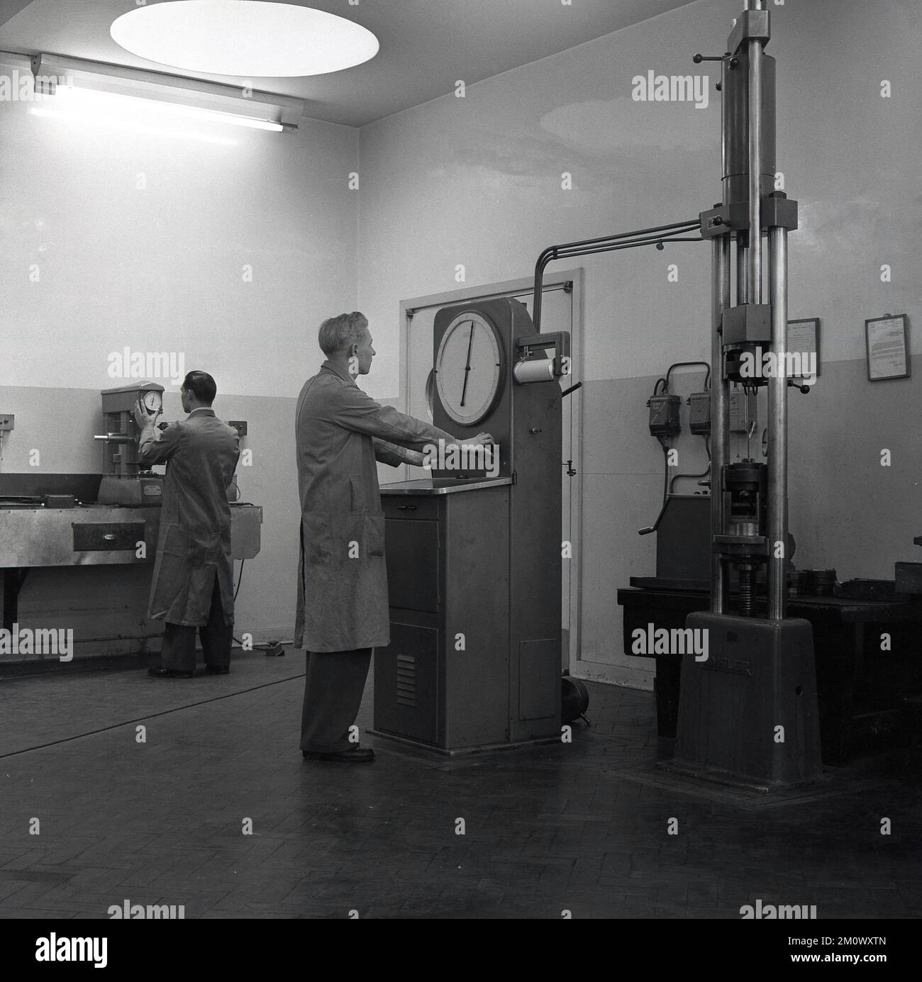 1950s, historique, steelworks, un long revêtement interne travaillant avec une machine de contrôle industrielle avec un grand cadran à l'Abbey Works, Port Talbot, sud du pays de Galles, Royaume-Uni. L'une des machines vues est fabriquée par Amsler, une société suisse qui a fabriqué des machines d'essai pour la tôle. Banque D'Images