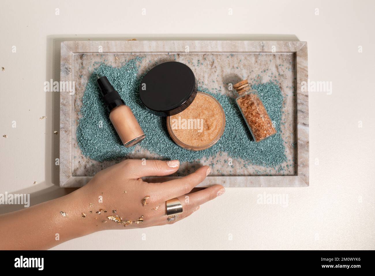 Femme non reconnaissable coupe courte main avec des sparkles dorés montrer plateau avec pot de sel de bain, poudre et maquillage beige cache-cache Banque D'Images