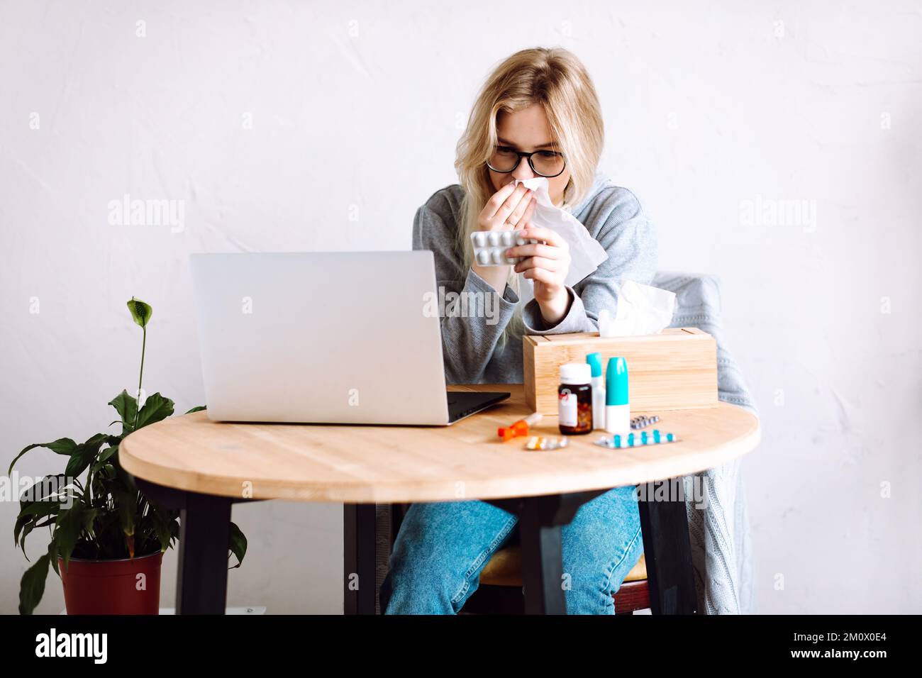 Portrait d'une jeune femme montrant des comprimés blister à l'écran, essuyant le nez courant, éternuant ayant appel vidéo avec le médecin. Banque D'Images
