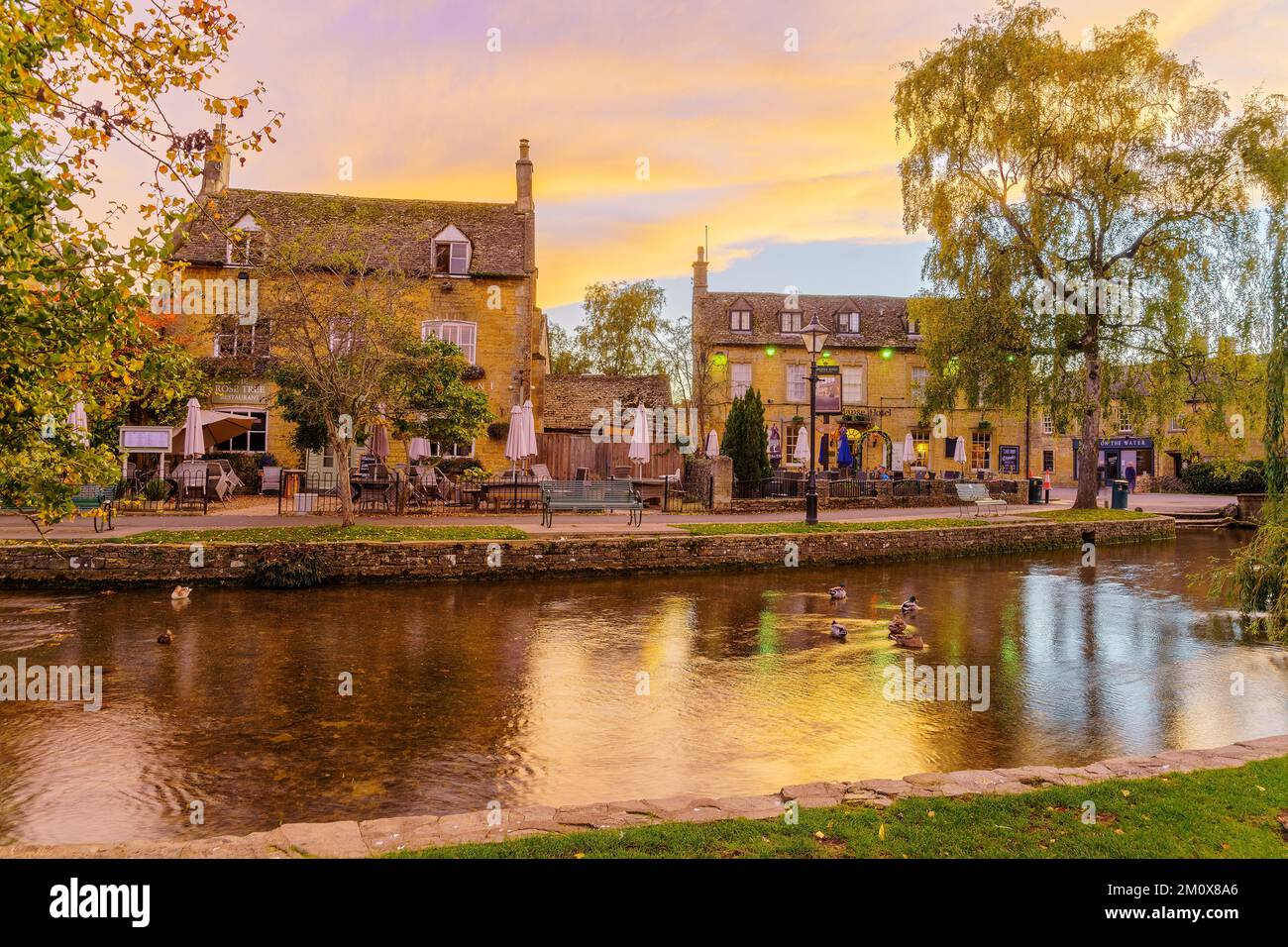 Bourton-sur-l'eau, Royaume-Uni - 17 octobre 2022 : scène de coucher de soleil de maisons typiques, la rivière Windrush, les habitants et les visiteurs, dans le village de Bourton-sur-l'eau Banque D'Images