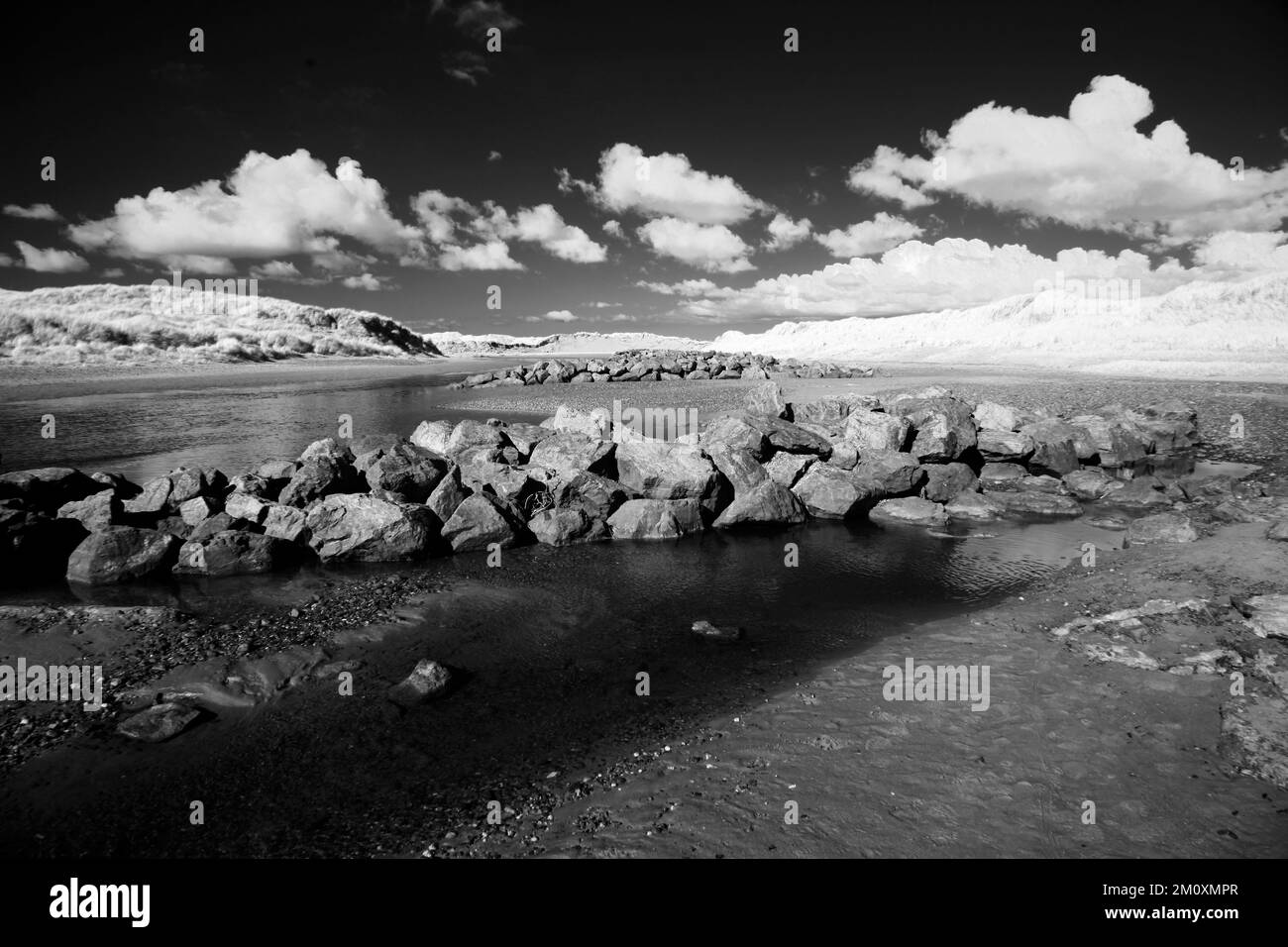 Photographie en noir et blanc de l'Afon Crigyll se déversant en mer avec des pauses marécageuses à Rhosneigr sur la côte ouest de l'île d'Anglesey, au nord du pays de Galles au Royaume-Uni, Banque D'Images