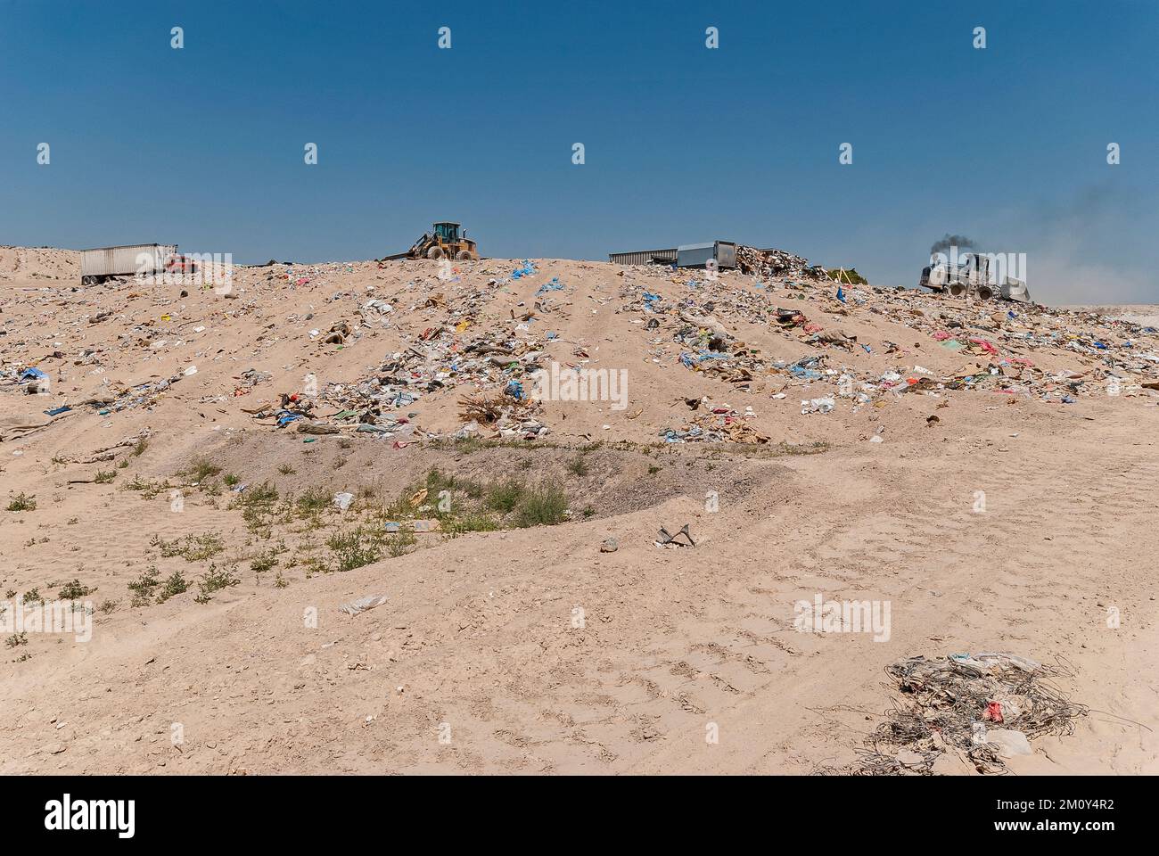 Un compacteur de sol émettant de la fumée diesel, un autre tracteur et plusieurs semi-remorques chargées de déchets dans une décharge active. Banque D'Images