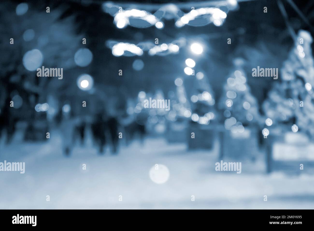 Résumé arrière-plan flou. Les gens qui marchent dans la rue des arbres de Noël décorés illuminés, illuminés et lumineux guirlandes dans la ville pendant les fortes chutes de neige la nuit d'hiver couleur bleue Banque D'Images