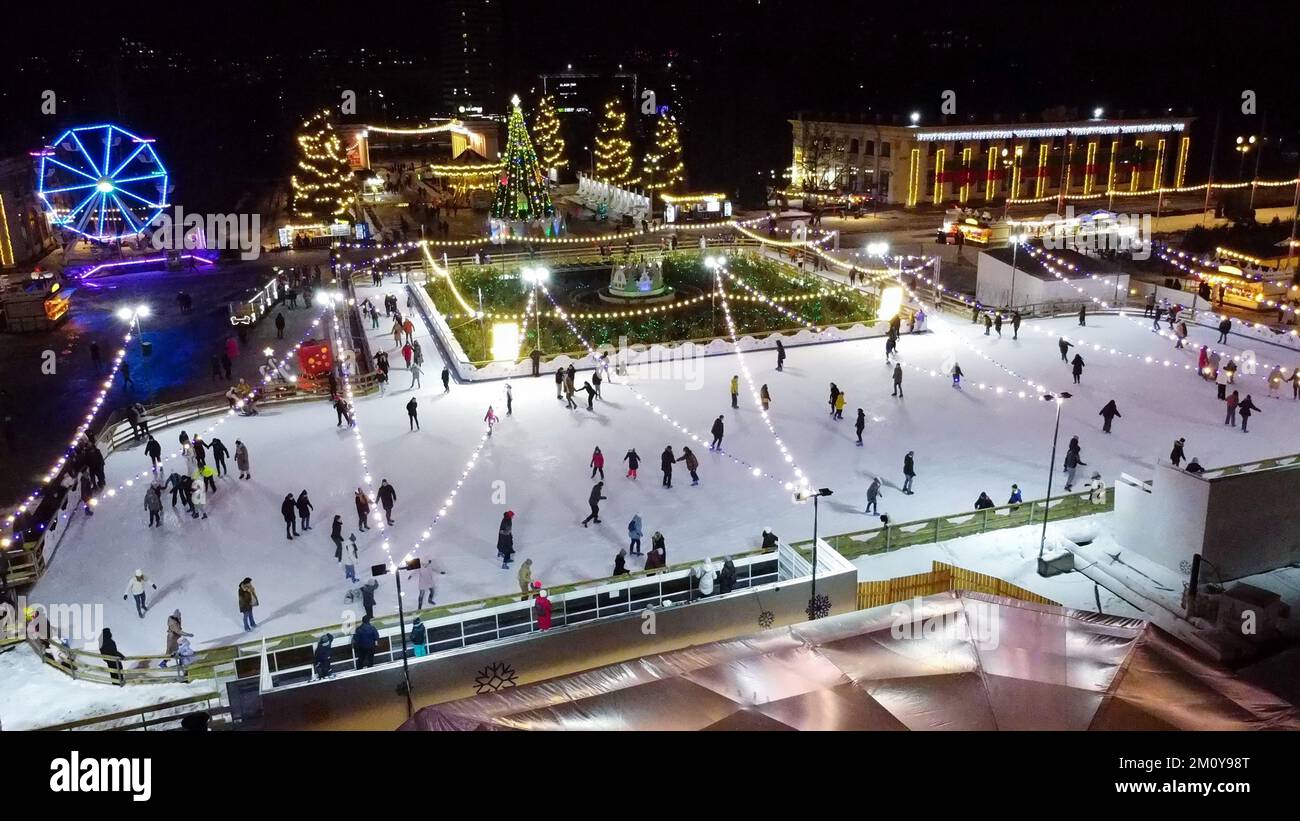 Beaucoup de personnes patinent sur la belle patinoire en plein air décorée illuminations de Noël du nouvel an, décorations, guirlandes lumineuses pendant la nuit d'hiver. Fête de Noël du nouvel an. Antenne Banque D'Images