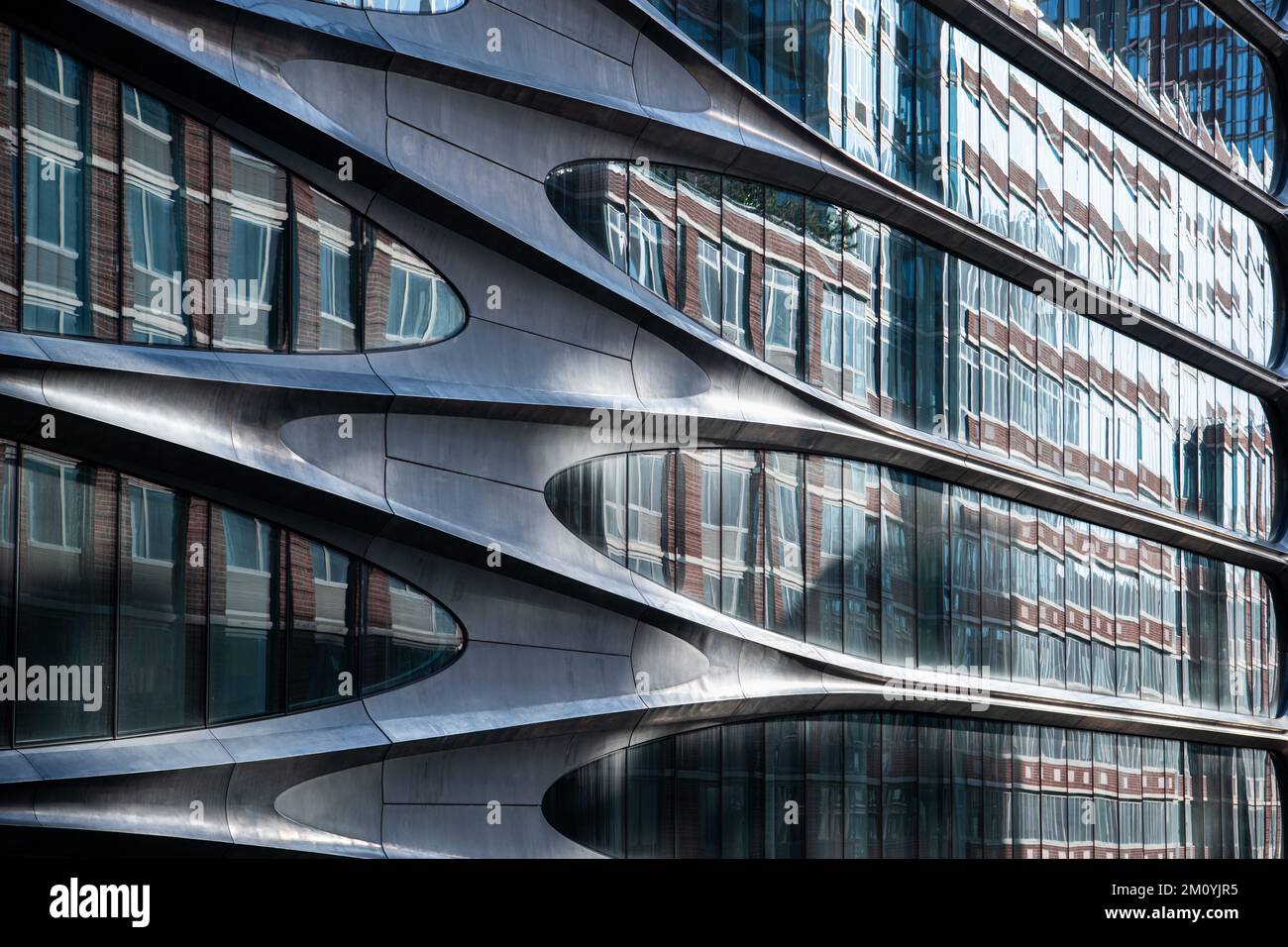 Les lignes courbes du revêtement métallique d'un bâtiment ultramoderne donnent sur des fenêtres en verre qui reflètent un bâtiment en brique Banque D'Images