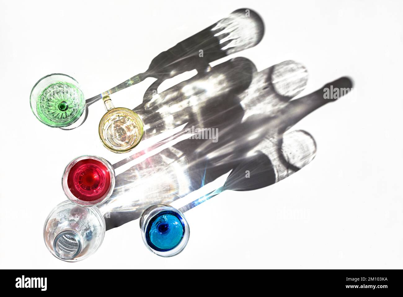Les verres à boire avec des liquides colorés et une bouteille d'eau jettent des ombres sur un fond lumineux, art abstrait, espace de copie, focus sélectionné, étroit Banque D'Images