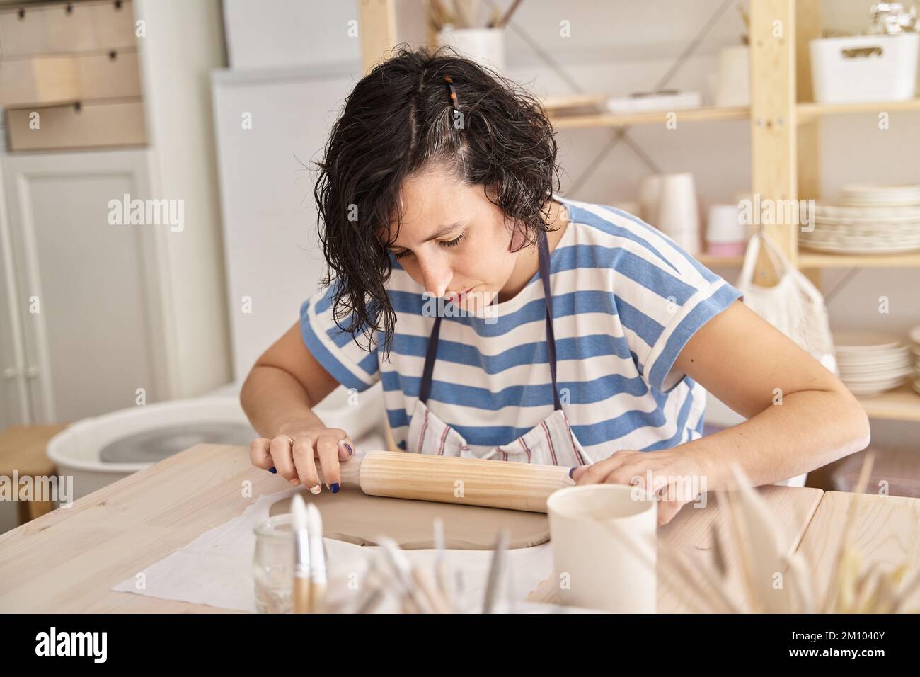 Femme en chemise rayée bleue pétrir de l'argile dans un atelier de poterie. Femme apprenant à travailler l'argile. Classe d'artisanat. Banque D'Images