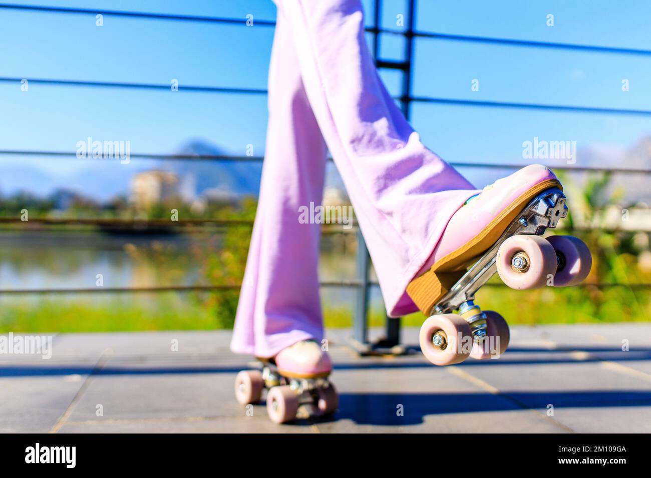 photo de près des pieds d'une femme dans un pantalon rose évasé patinant sur des rouleaux dans le parc Banque D'Images