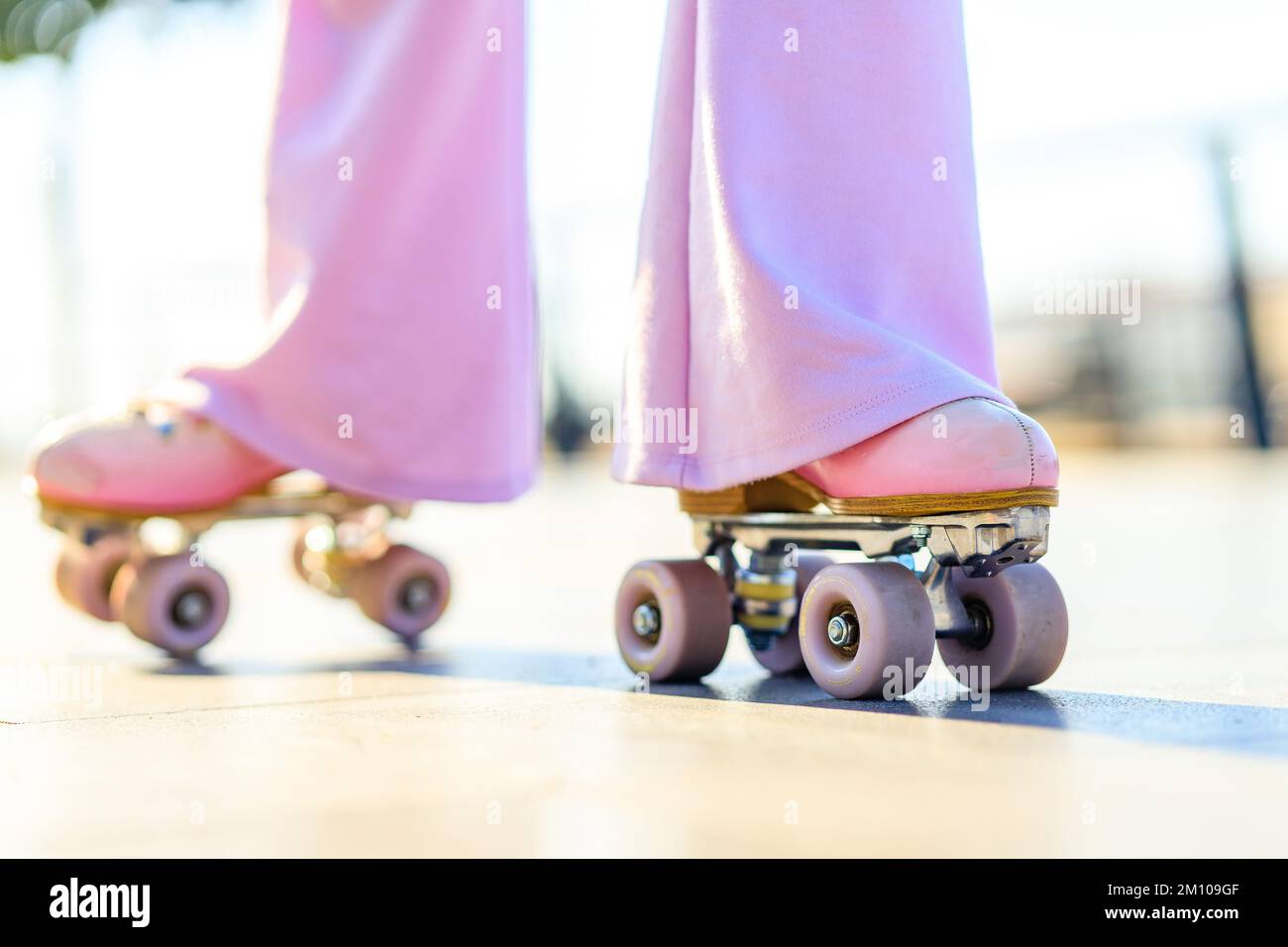 gros plan de jambes femme dans un pantalon à fond de cloche avec patins à roulettes rose pastel à l'extérieur par beau temps Banque D'Images