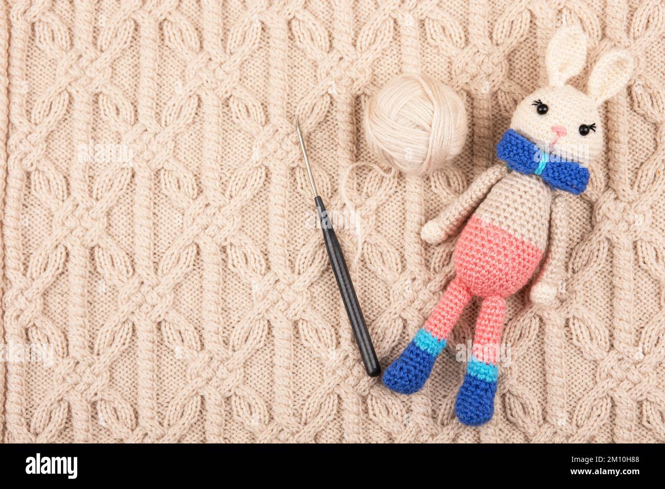 Un jouet en bonneterie lièvre ou lapin avec une boule de fil et un crochet en crochet sur un tissu beige tricoté. Le symbole de 2023. Banque D'Images