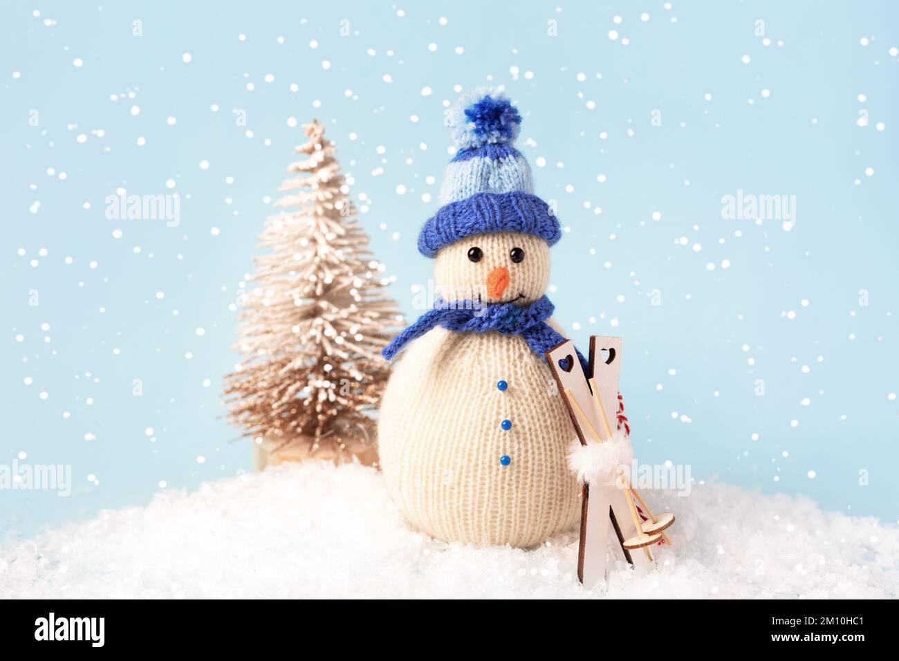 Composition de Noël d'un bonhomme de neige tricoté dans un chapeau bleu et une écharpe avec skis sur le fond d'un petit arbre de Noël Banque D'Images