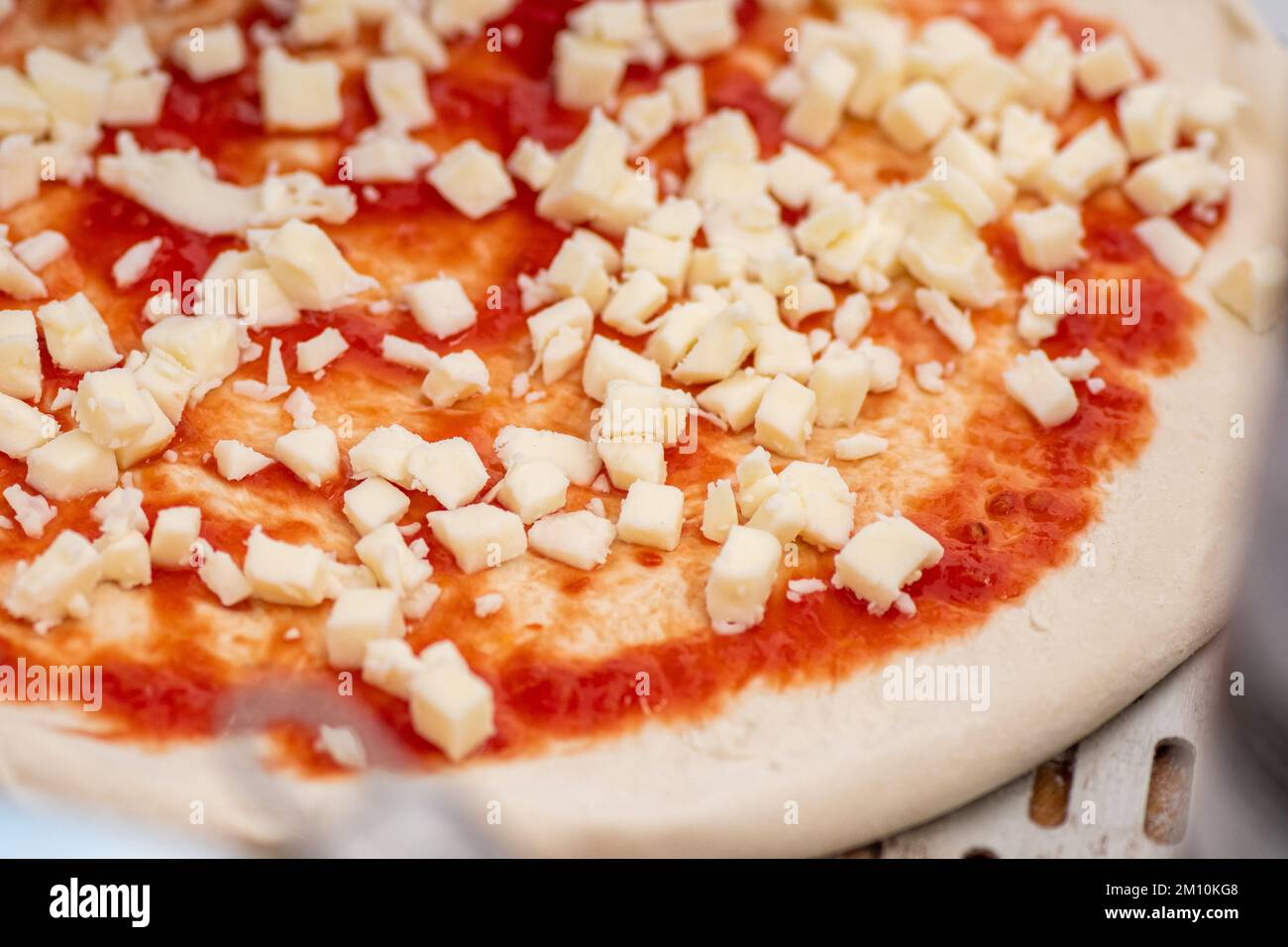Préparer une pizza avec une sauce tomate et de la mozzarella fraîche sur une planche de bois avec des ingrédients et des outils autour, gros plan Banque D'Images