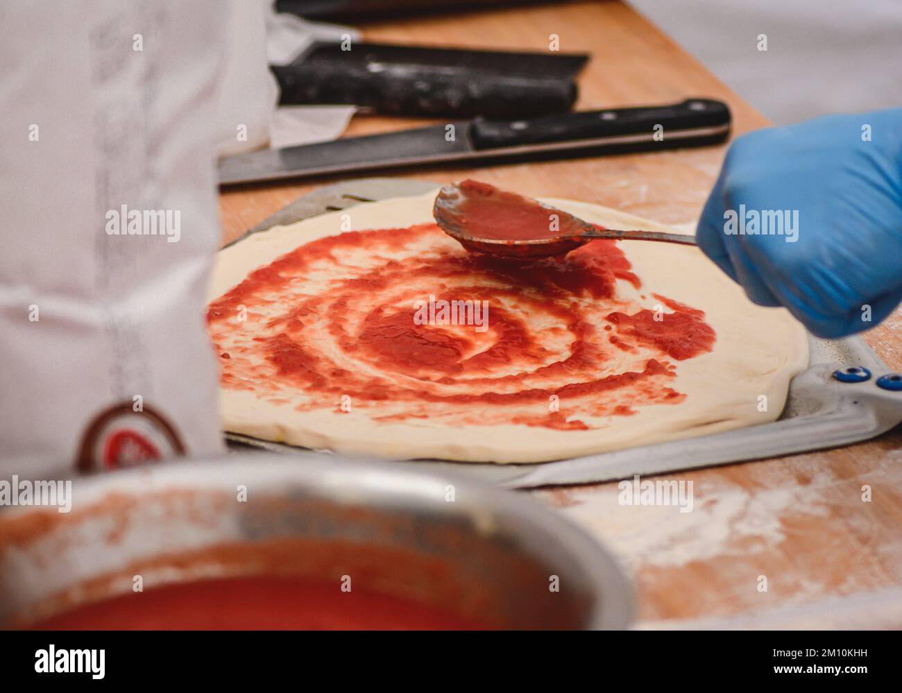 Ajouter la sauce tomate avec une cuillère sur la pâte à pizza sur une pelle sur un panneau en bois, gros plan Banque D'Images