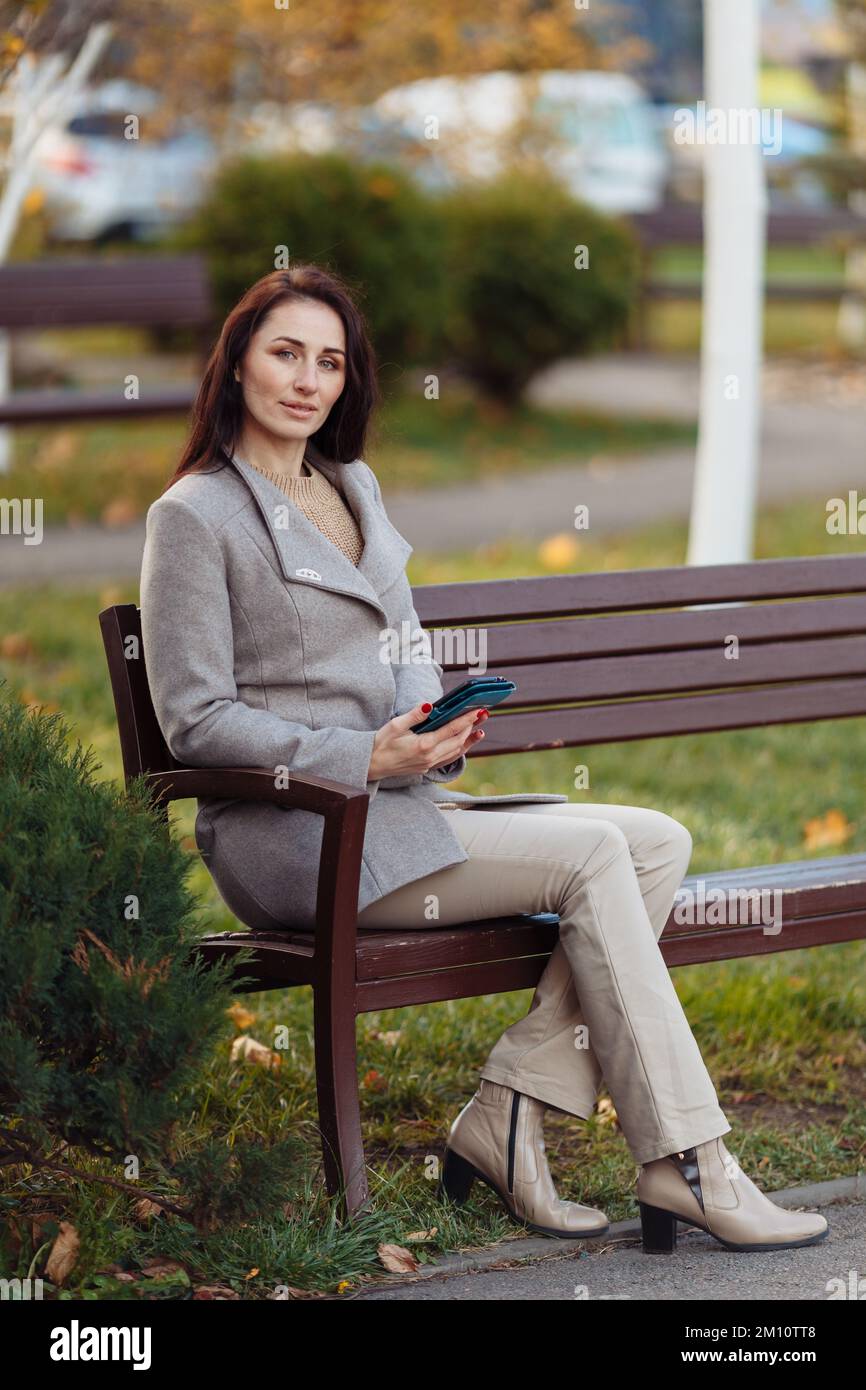 Femme assise sur l'herbe au parc travaillant sur un ordinateur portable. Une femme porte des écouteurs sur un ordinateur portable tout en étant assise sous un arbre au parc, avec une lumière vive de l'arrière. Photo de haute qualité Banque D'Images
