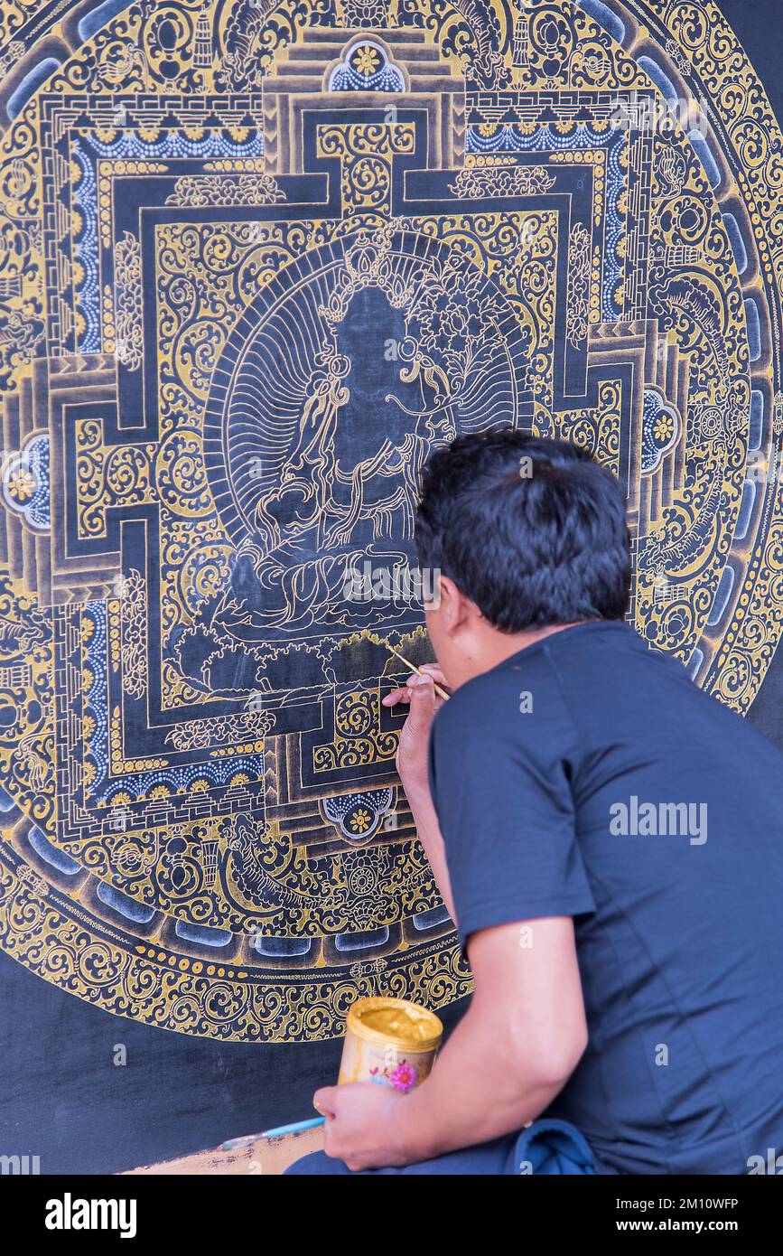 Un artisan peint un mandala bouddhiste dans un village le long de la route transhubhoutanique. Banque D'Images