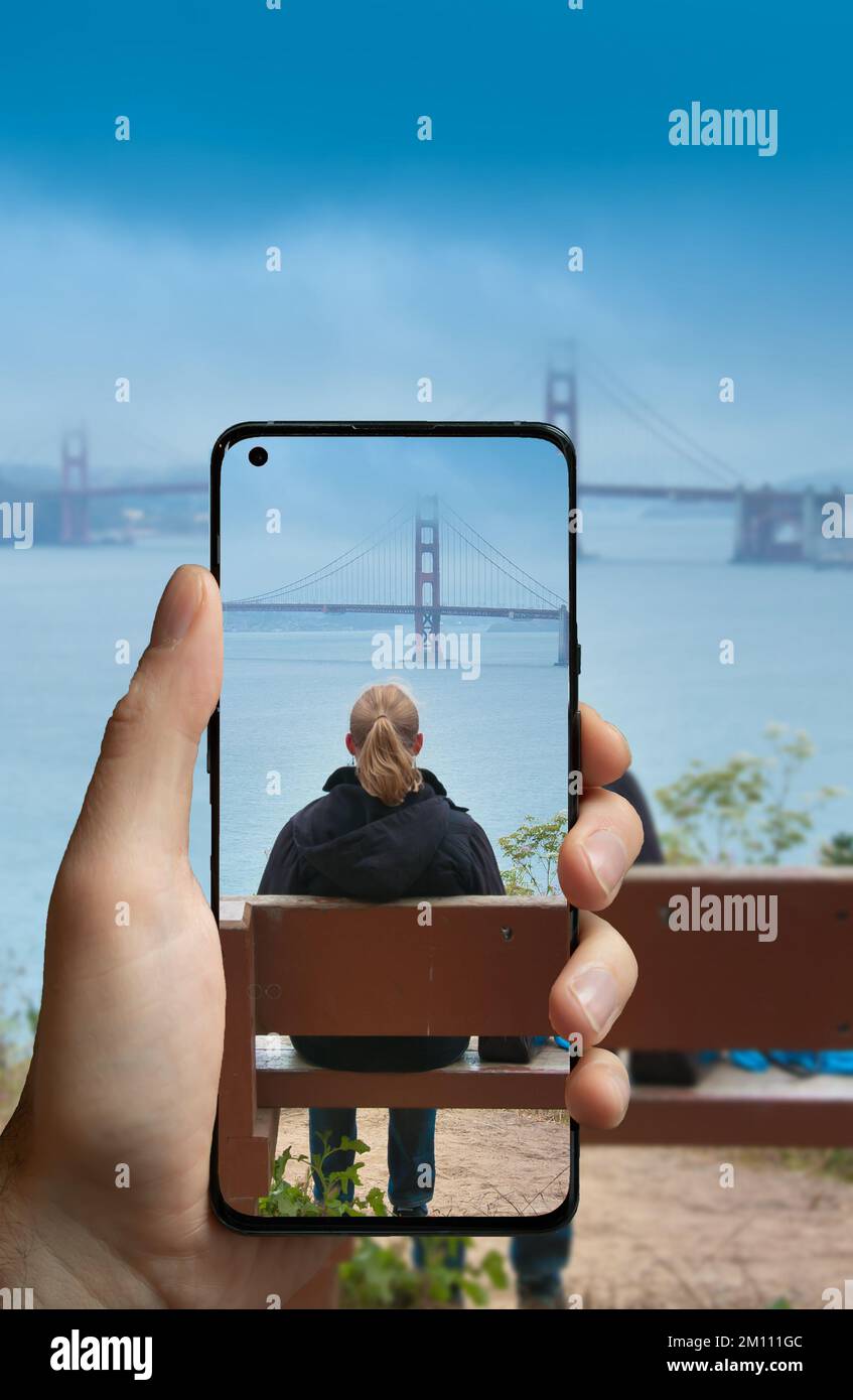 Prendre une photo avec un téléphone portable d'une femme assise sur un banc et regardant le Golden Gate Bridge à San Francisco, aux États-Unis. Banque D'Images
