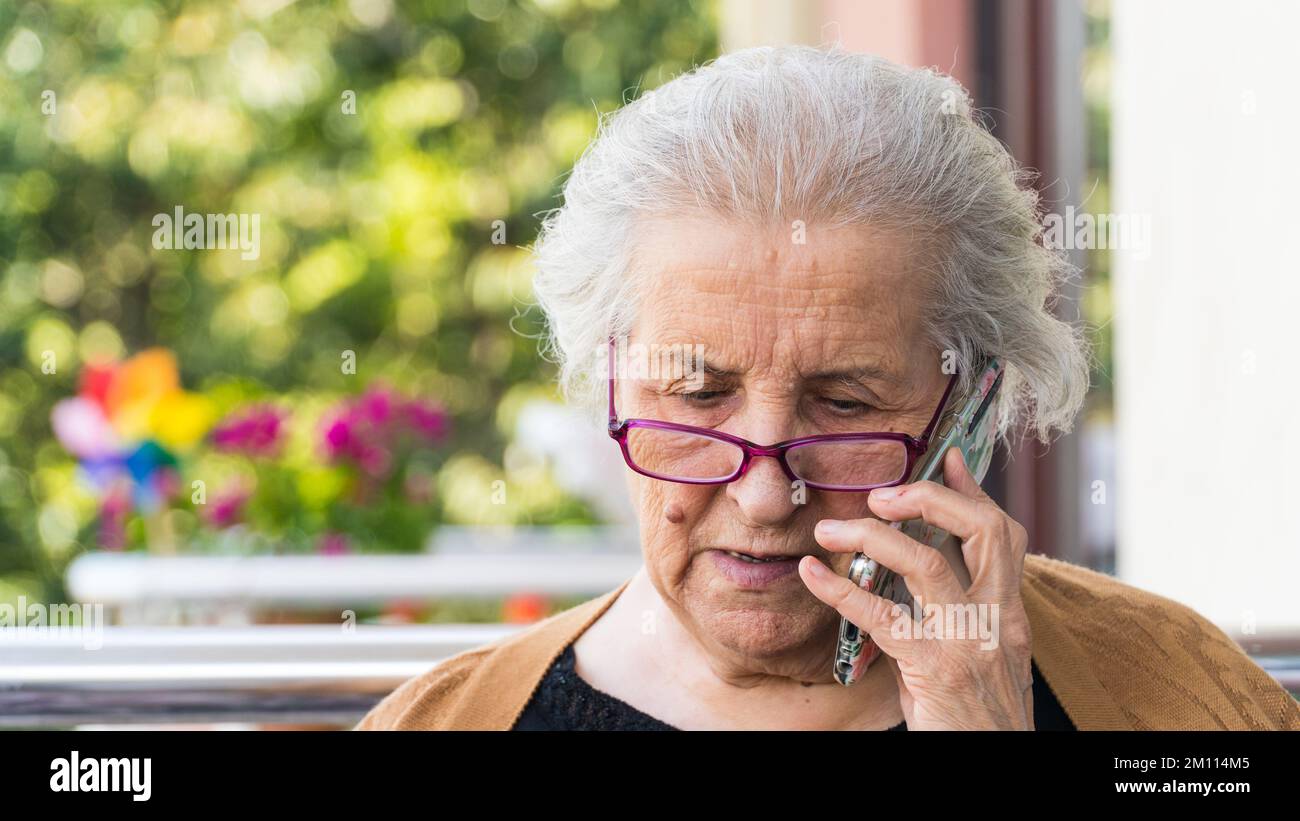 Vieille femme avec des lunettes parlant au téléphone. La vieille femme entend de mauvaises nouvelles au téléphone et fait triste impression de visage. Banque D'Images