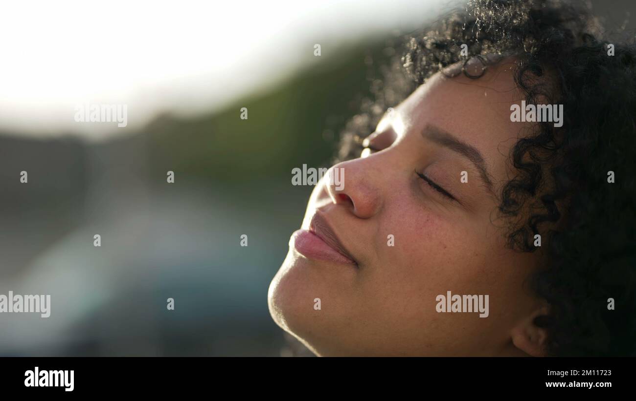 Une jeune femme noire regardant le ciel fermer les yeux dans la contemplation. Femme sentant le vent de la brise dans la méditation. hisp sud-américain contemplatif Banque D'Images