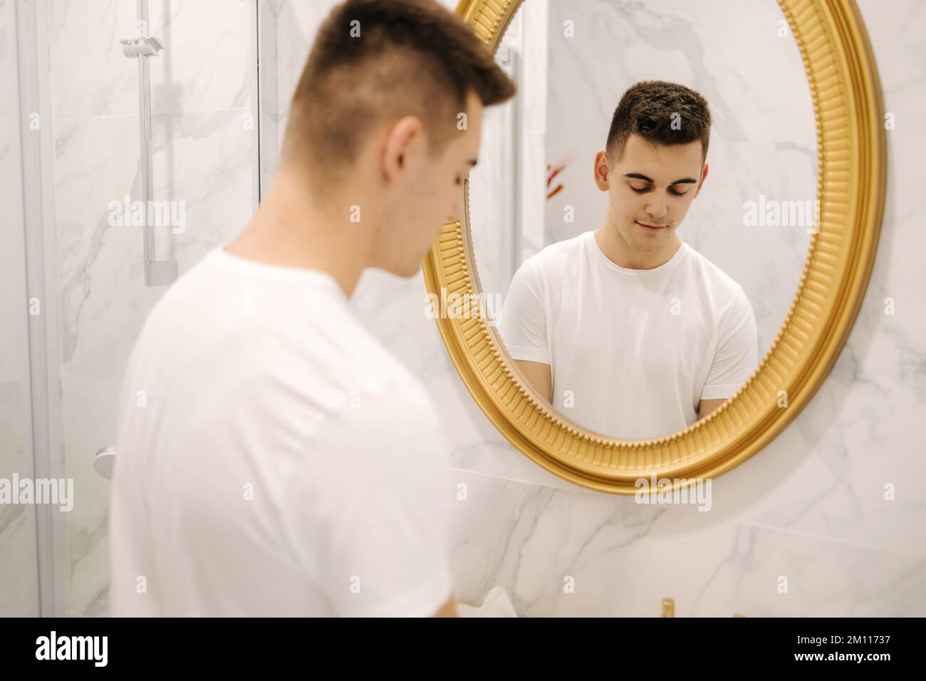 Jeune homme beau en t-shirt blanc dans le bain. Mise au point dans le miroir Banque D'Images