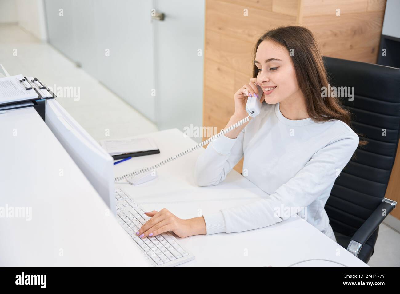 Une secrétaire joyeuse parlant au téléphone à la réception Banque D'Images
