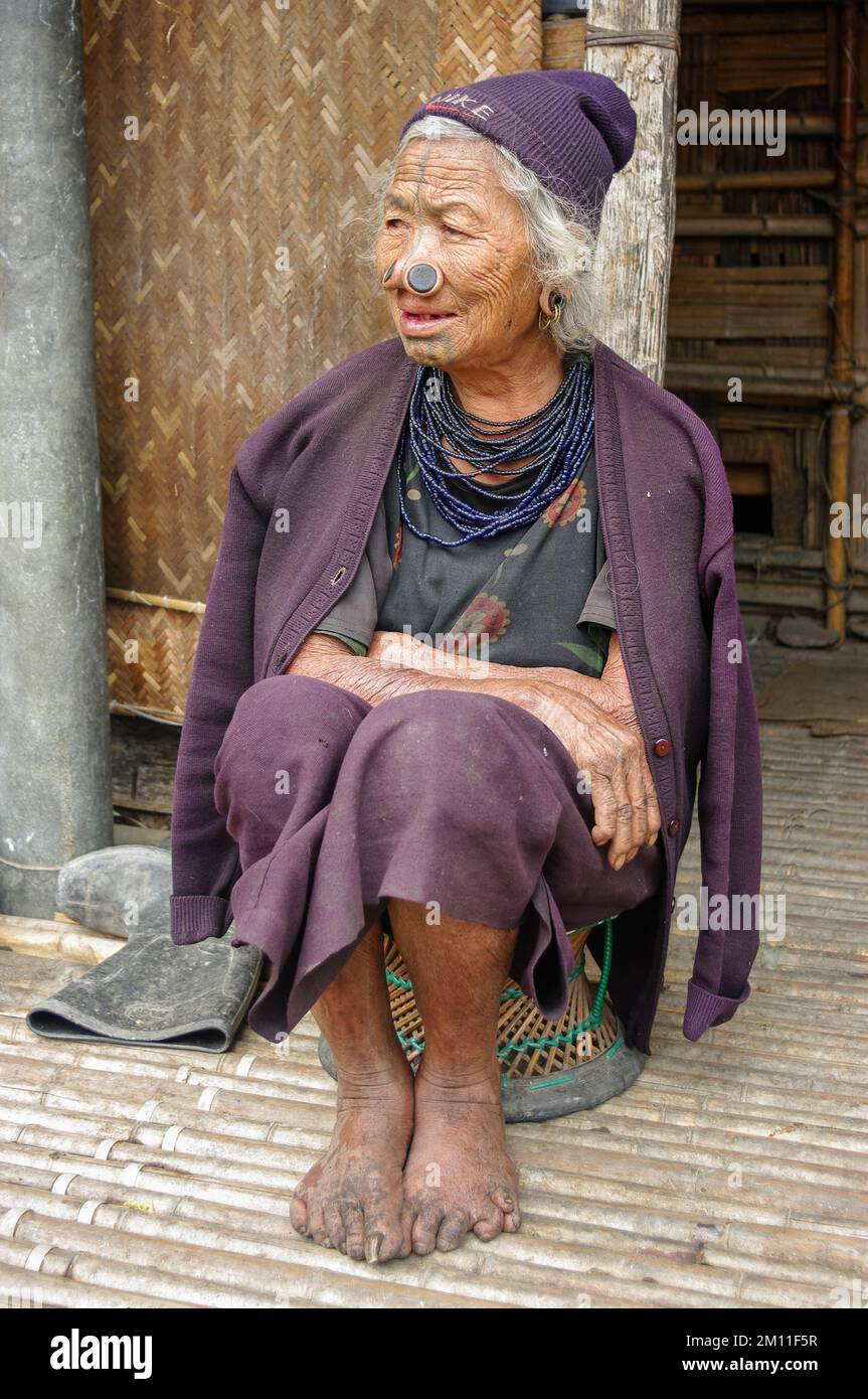 Ziro, Arunachal Pradesh, Inde - 02 24 2009 : Portrait de la vieille femme tribale d'Apatani avec des tatouages faciaux traditionnels et des prises de nez assis sur un tabouret Banque D'Images