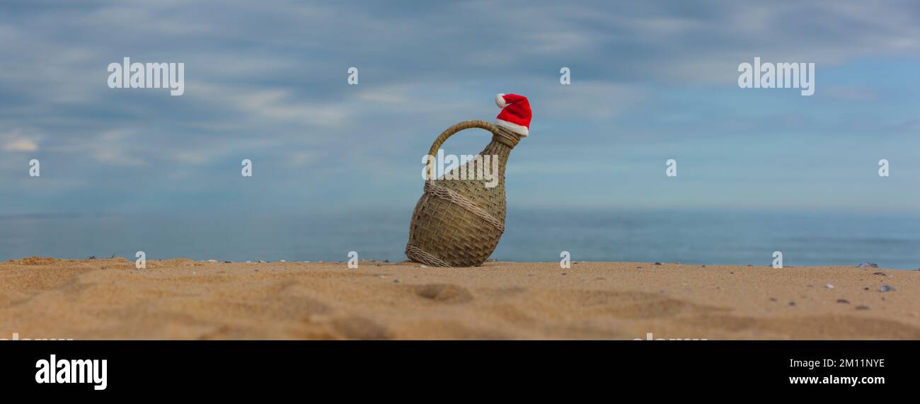 Vieille carafe à vin avec chapeau du Père Noël sur la plage Banque D'Images