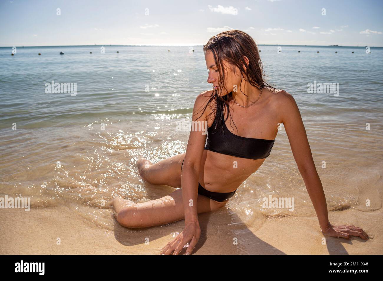 Jeune femme modèle en maillot de bain sexy posant sur l'une des plages de l'île Maurice à la lumière du coucher du soleil. Poils ondulés Pertfect, corps SKIM bronzé. Ambiance tropicale d'été. Banque D'Images