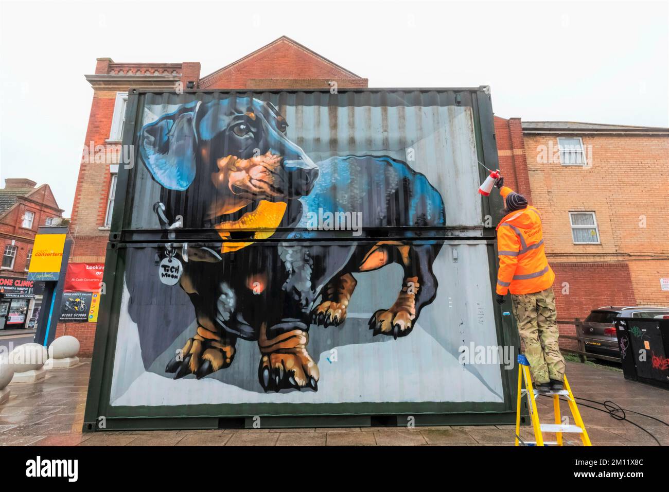 Angleterre, Dorset, Bournemouth, Boscombe, Council Worker Cleaning Street Art intitulé « The Sausage Dog » par l'artiste Tech Moon Banque D'Images