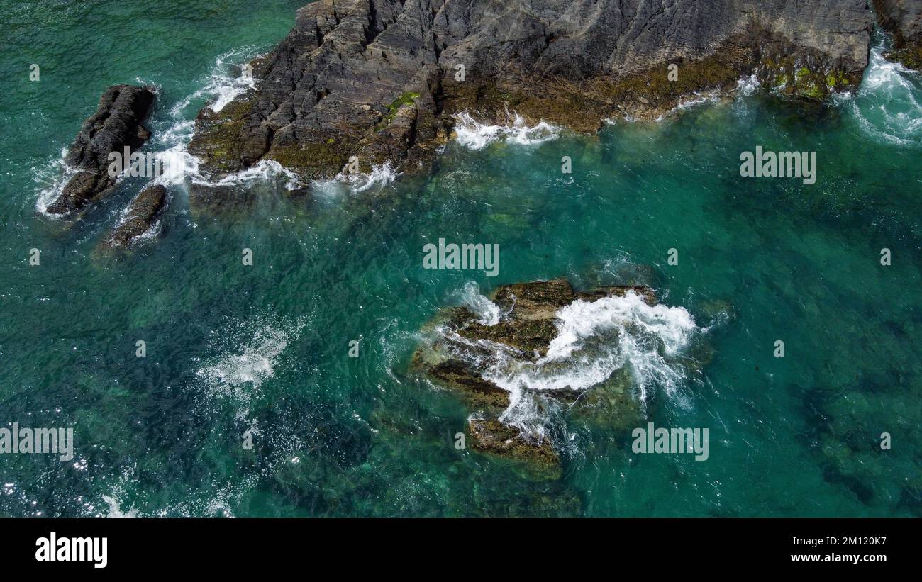 Rochers couverts de mousse noire au milieu des vagues turquoise de la mer celtique. Mousse de mer blanche sur les vagues. Eaux de l'océan Atlantique. Photo aérienne. Banque D'Images