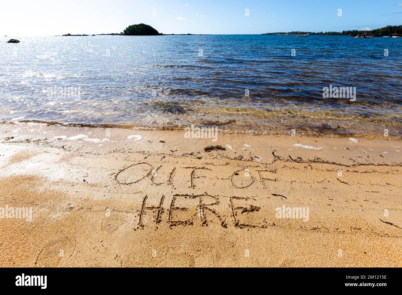 Hors d'ici - comme un message écrit avec un doigt dans le sable sur une plage avec des vagues et l'océan bleu à l'île Maurice, l'Afrique, vue de dessus, personne Banque D'Images