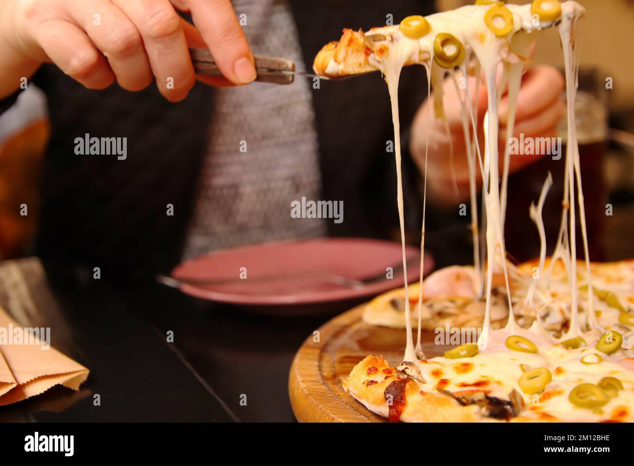 Défpoint main femelle tenant une tranche de pizza italienne tortilla avec Mozzarella râpé. Pizza aux olives, basilic et fromage en gros plan. Pizzeria à l'extérieur Banque D'Images