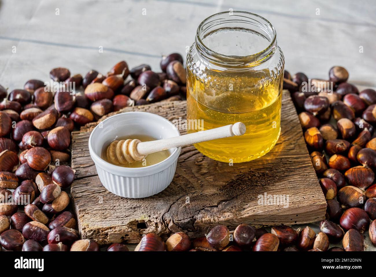 jarre de miel d'abeille avec petite tasse et un balancier de miel sur panneau en bois antique, atmosphère d'automne avec châtaignes Banque D'Images