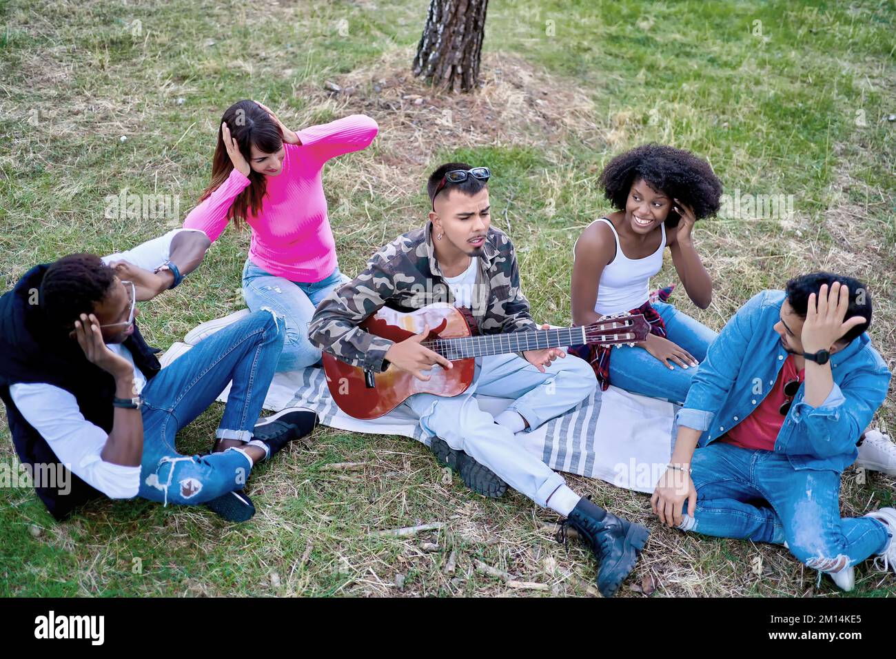 Amis multiethniques assis sur le terrain tandis que l'on joue de la guitare dans un parc. Concept d'amitié. Banque D'Images
