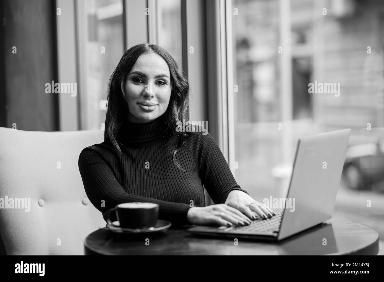 Femme d'affaires assise à une table dans le bureau, travaillant sur un ordinateur portable et buvant du café. Banque D'Images