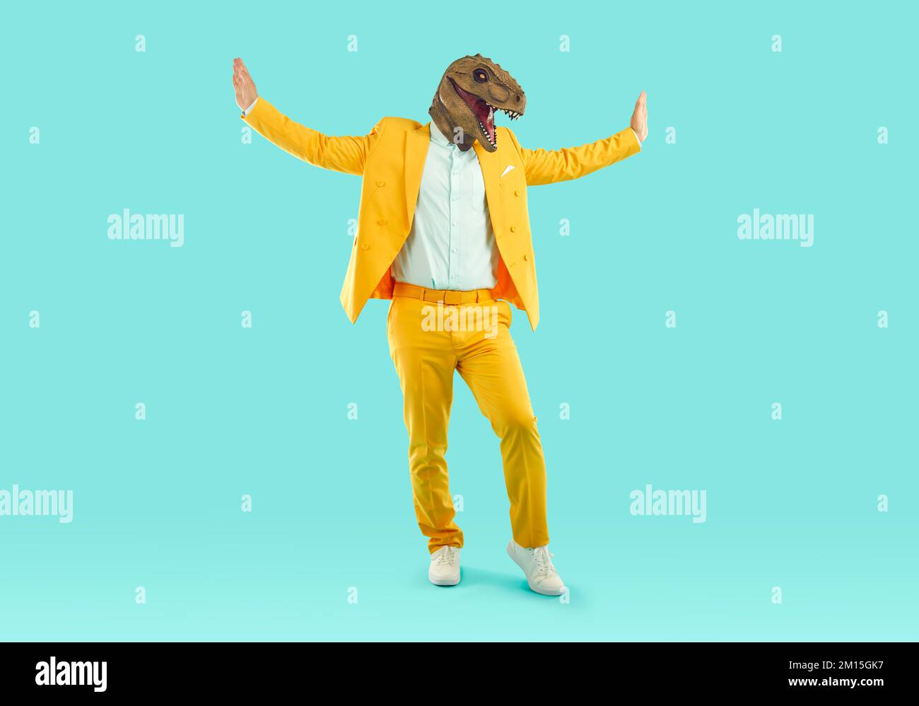 Portrait d'un homme joyeux et stylé dans un masque de dinosaure en caoutchouc tendance qui danse et se berce. Banque D'Images