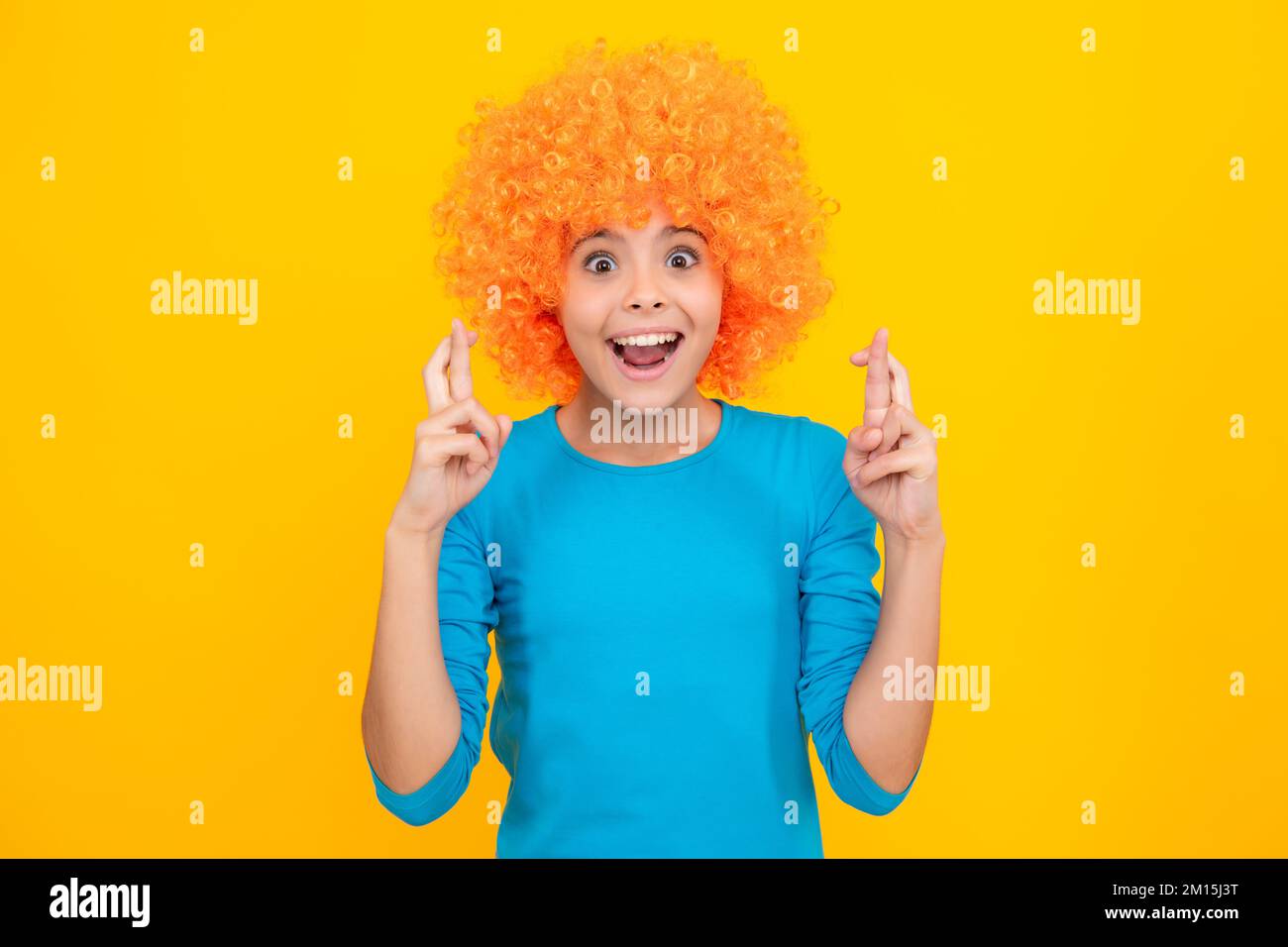 Anniversaire fête d'enfants. Drôle d'enfant dans la perruque clown curly isolé sur fond jaune. Banque D'Images