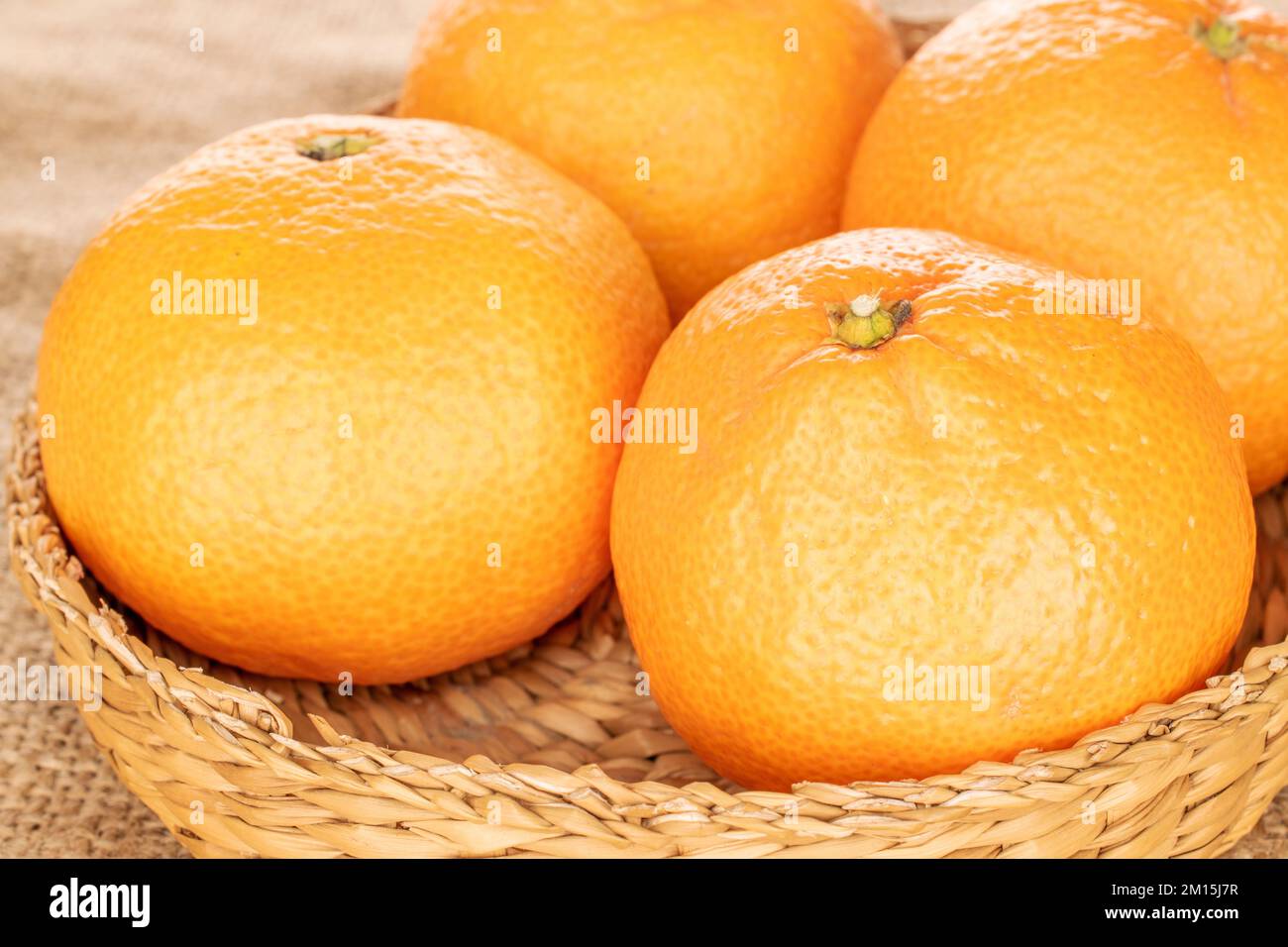 Quelques mandarines mûres dans une plaque de paille sur un chiffon de jute, macro. Banque D'Images