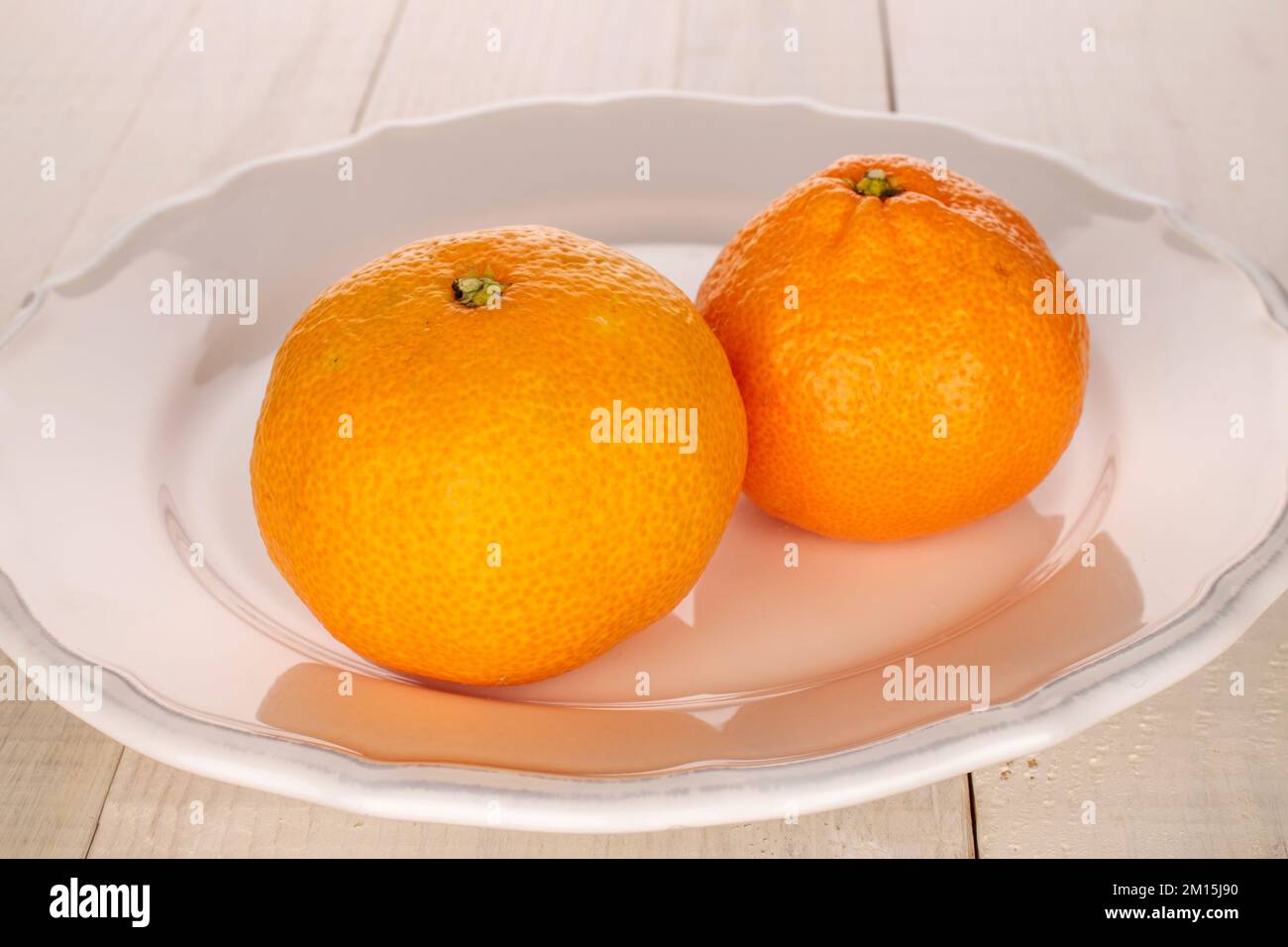 Deux mandarines mûres dans une plaque blanche sur une table en bois, macro. Banque D'Images