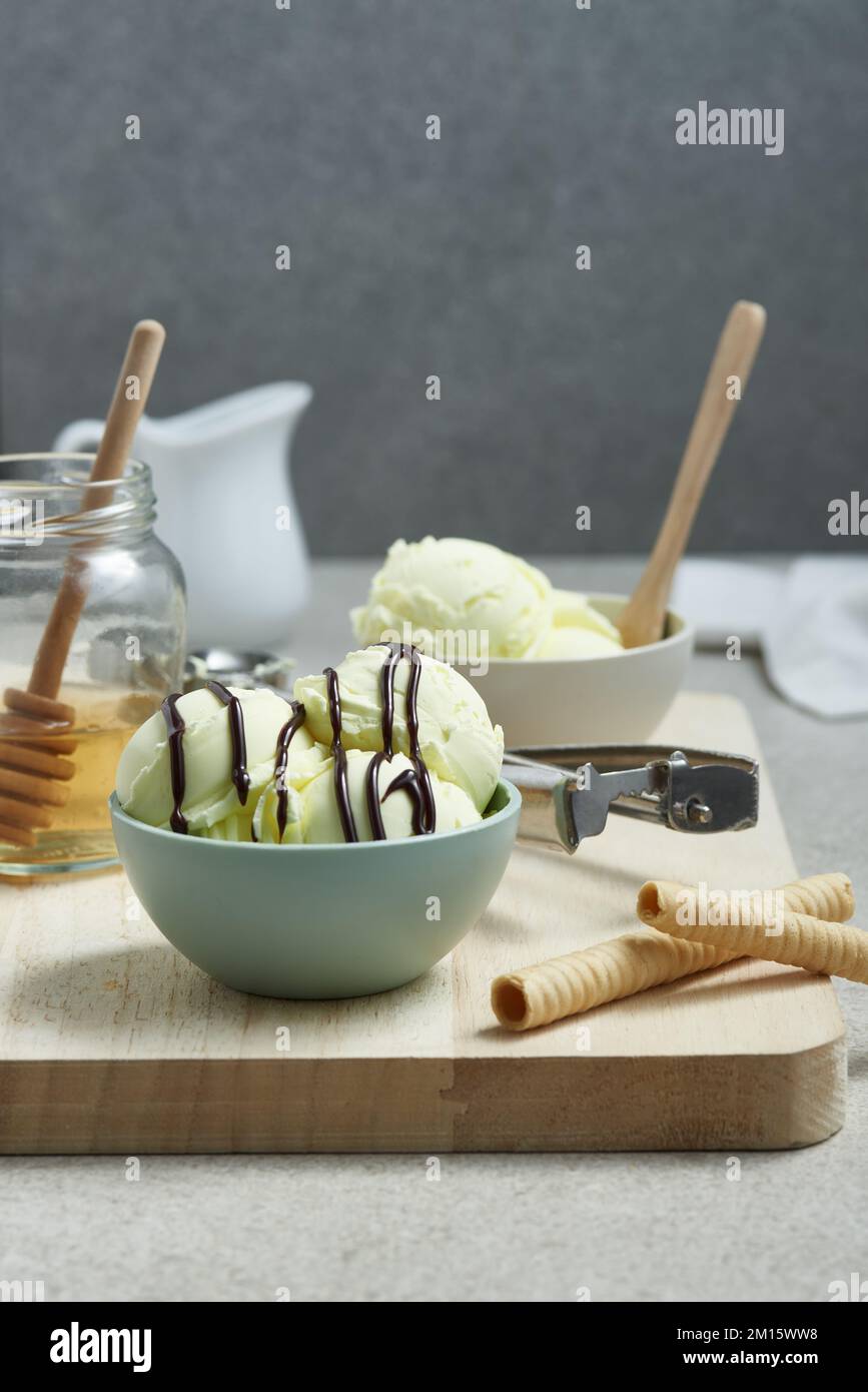 Une délicieuse crème glacée dans un bol recouvert de sauce au chocolat et servie sur un plan de coupe en bois avec un pot de miel et des rouleaux de gaufres dans la cuisine Banque D'Images