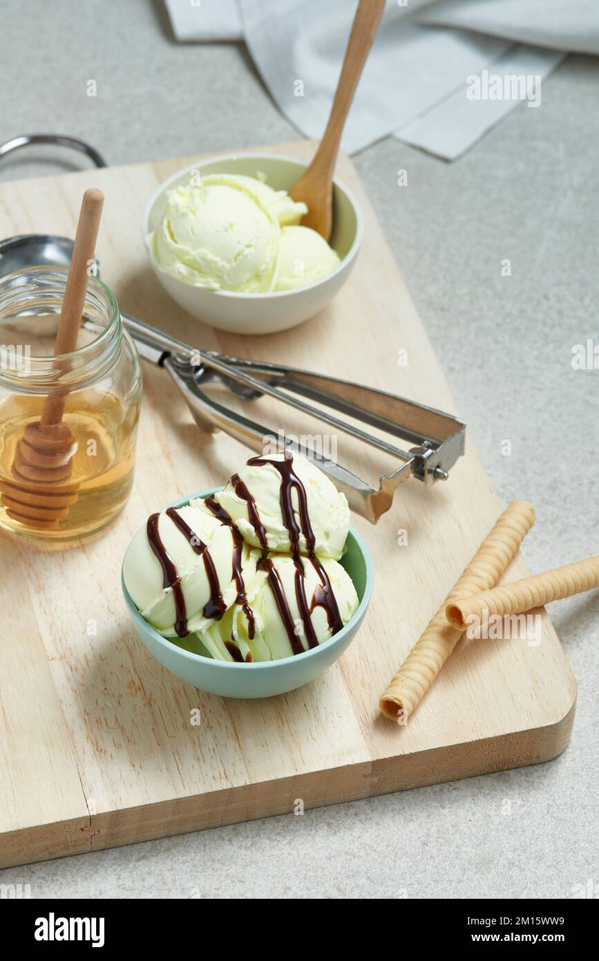 Au-dessus de la glace délicieuse, des pelles dans un bol recouvert de sauce au chocolat et servi sur un plateau de découpe en bois avec un pot de miel et des rouleaux de gaufres dans le kitc Banque D'Images