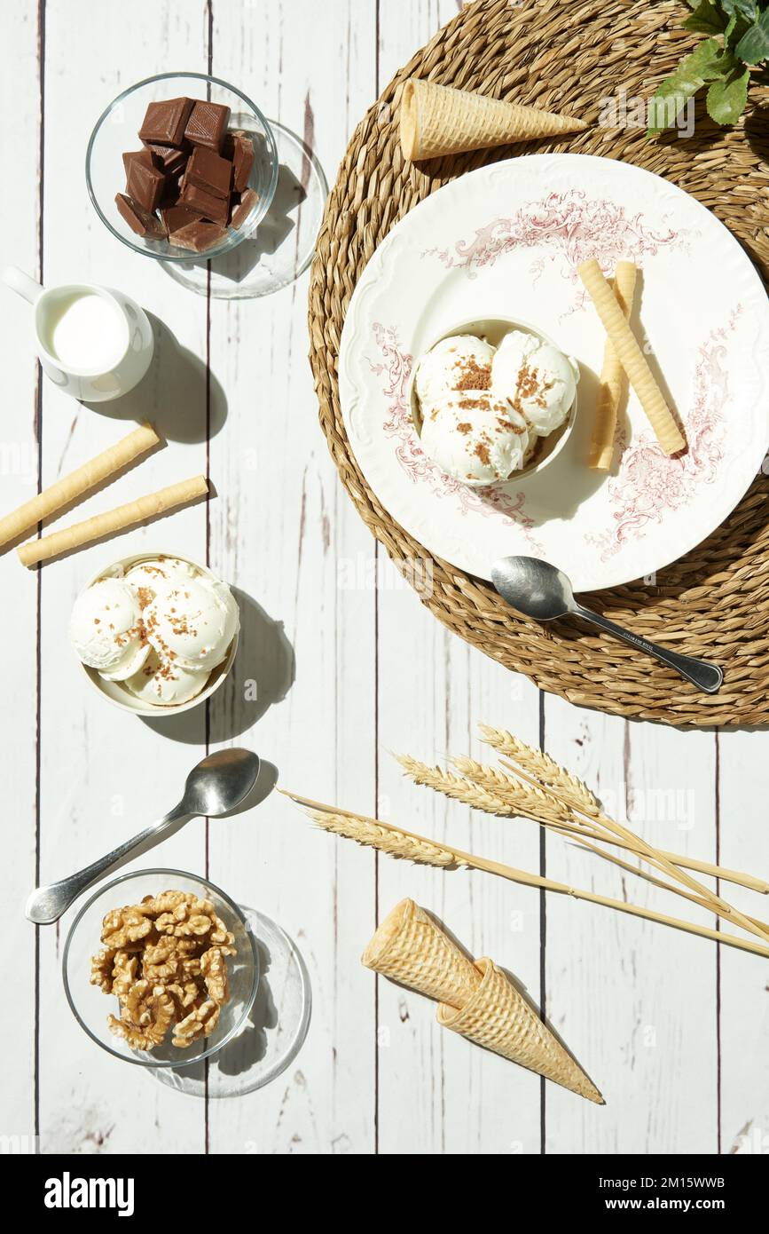 Au-dessus de la délicieuse crème glacée servie dans des bols avec des rouleaux de gaufres et des cônes et placée sur une table en bois blanc près du pichet avec des barres de chocolat au lait a Banque D'Images