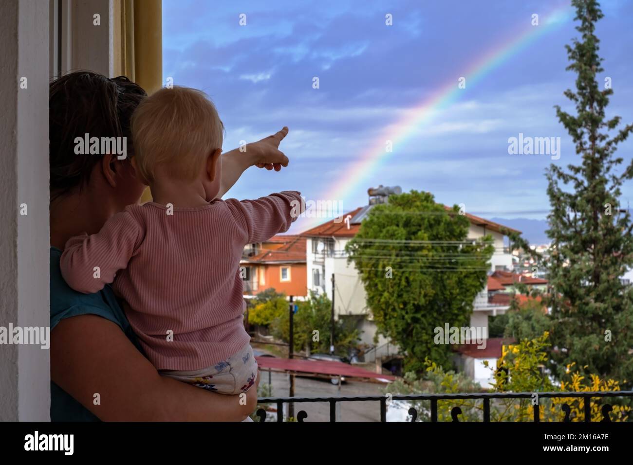 Mère regarde le ciel avec un bébé dans ses bras, admire l'arc-en-ciel Banque D'Images