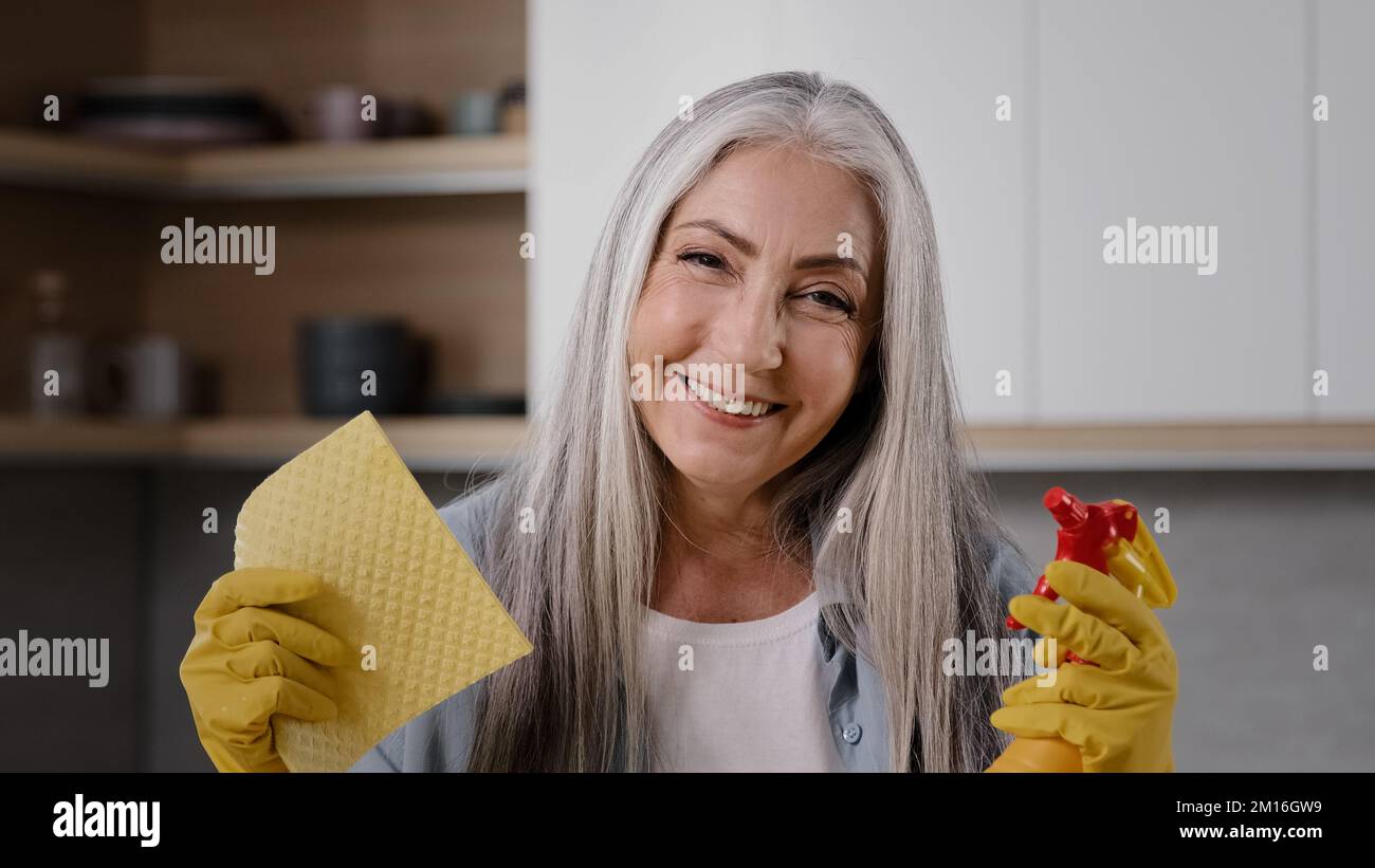 Bonne femme travailleur propre grand-mère caucasienne ancienne posant pour caméra en caoutchouc jaune gants tenir dans les mains chiffon et vaporisateur bouteille avec liquide propre Banque D'Images